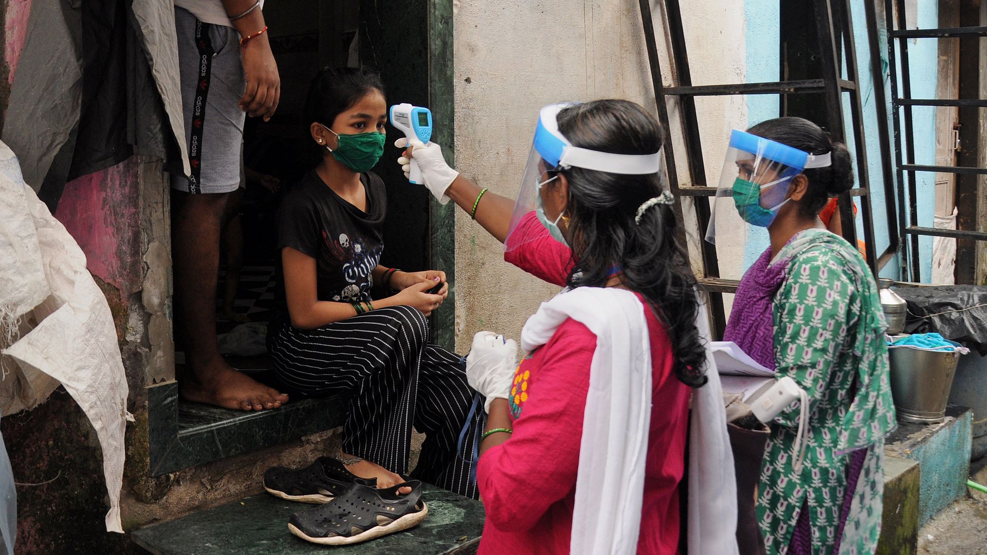 Healthcare worker wearing a face shield checks the temperature of a girl. 