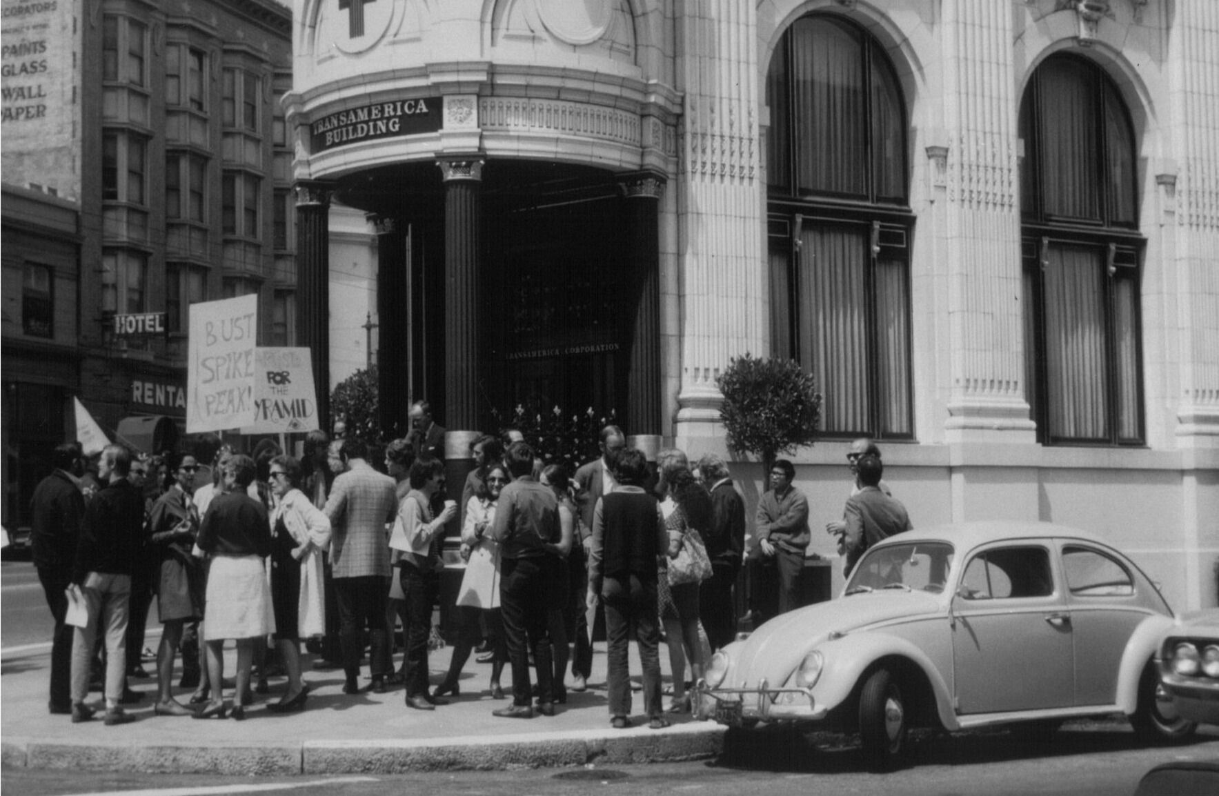 Black and white photo of people clustered around a building holding signs against the Pyramid's construction