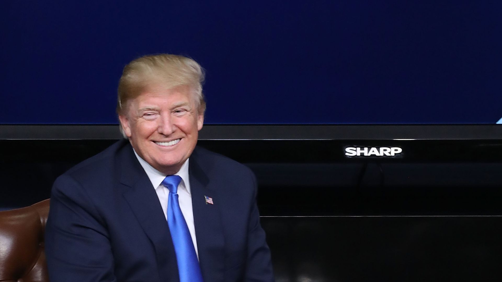 Donald Trump smiling and sitting next to a wooden table with plastic water bottles on it