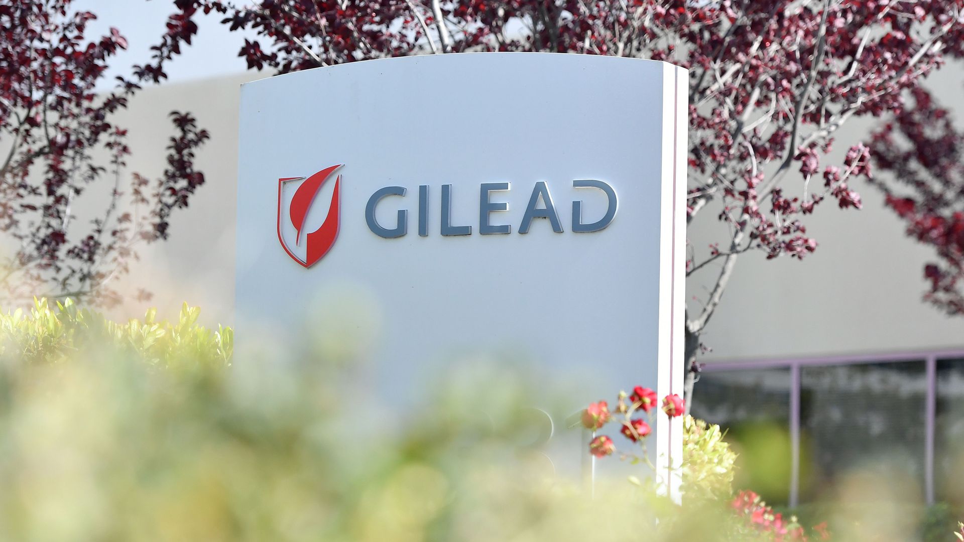 The Gilead logo on a sign surrounding by flowers and trees.