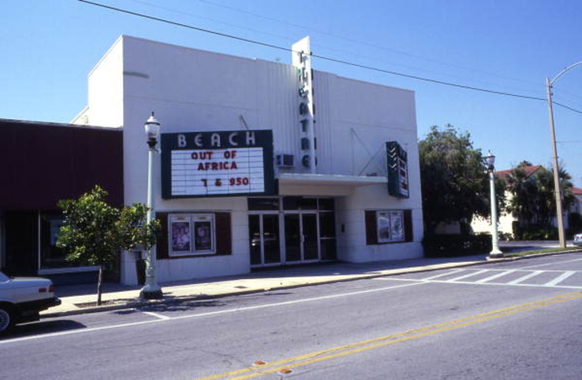 A white art-deco building with marquees that read "BEACH" above them and a sign that says "THEATRE." The marquee advertises "Out of Africa" showings at 7 and 9:30.