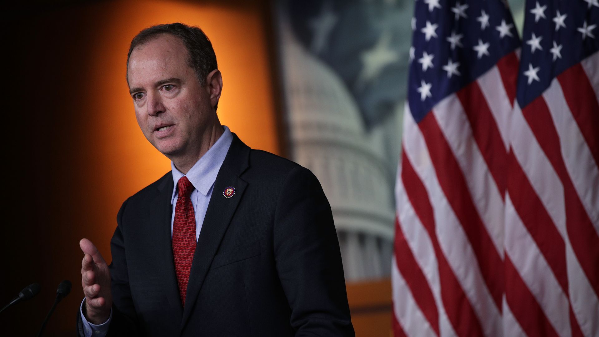 Adam Schiff stands next to a flag gesturing with a hand while speaking. 