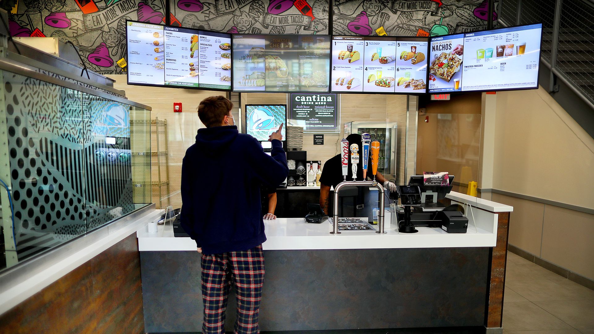 A person stands at a fast-food counter peering up at a digital menu.