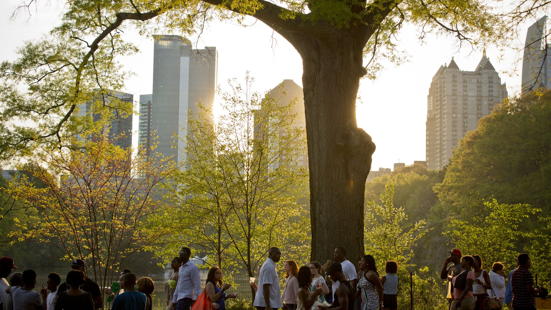 A photo of people walking around a large festival in a public park as the sun starts to set against a skyline backdrop