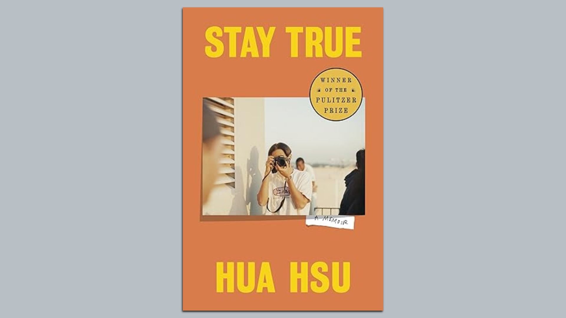 Book cover of "Stay True" by Hua Hsu, orange background with yellow text, features a photo of a person holding a camera. Includes a Pulitzer Prize winner gold medal.
