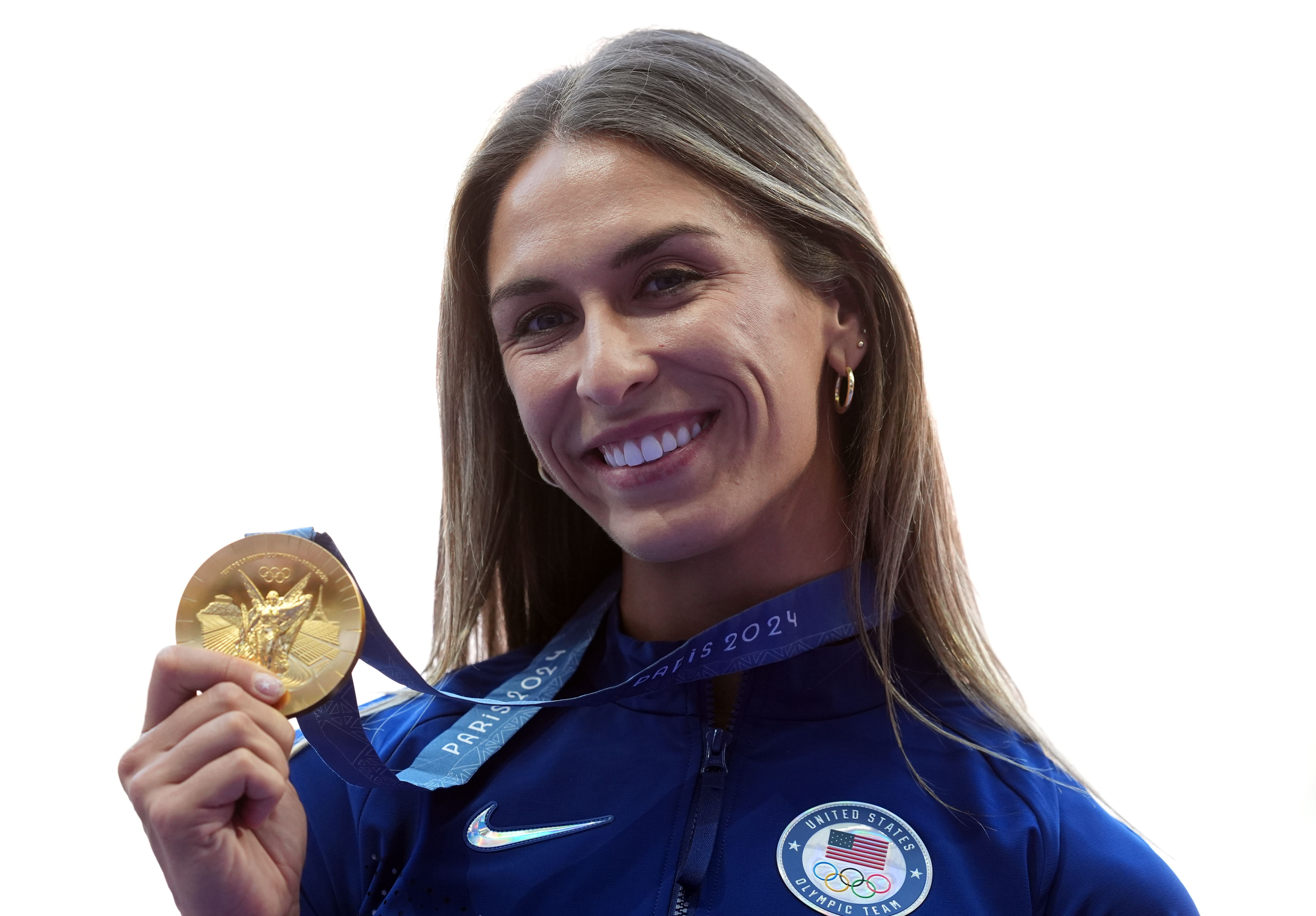 A woman holds up a gold medal while smiling. 