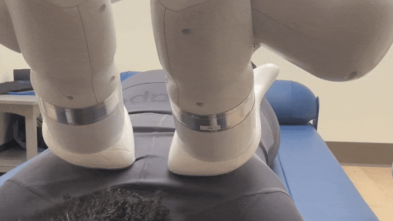 Two robot arms massage the back of a woman lying down, wearing black