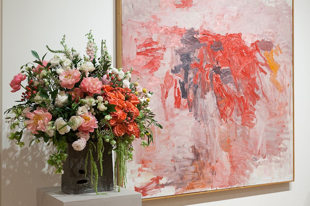 A large vase of pink and red flowers next to a pink and red painting.