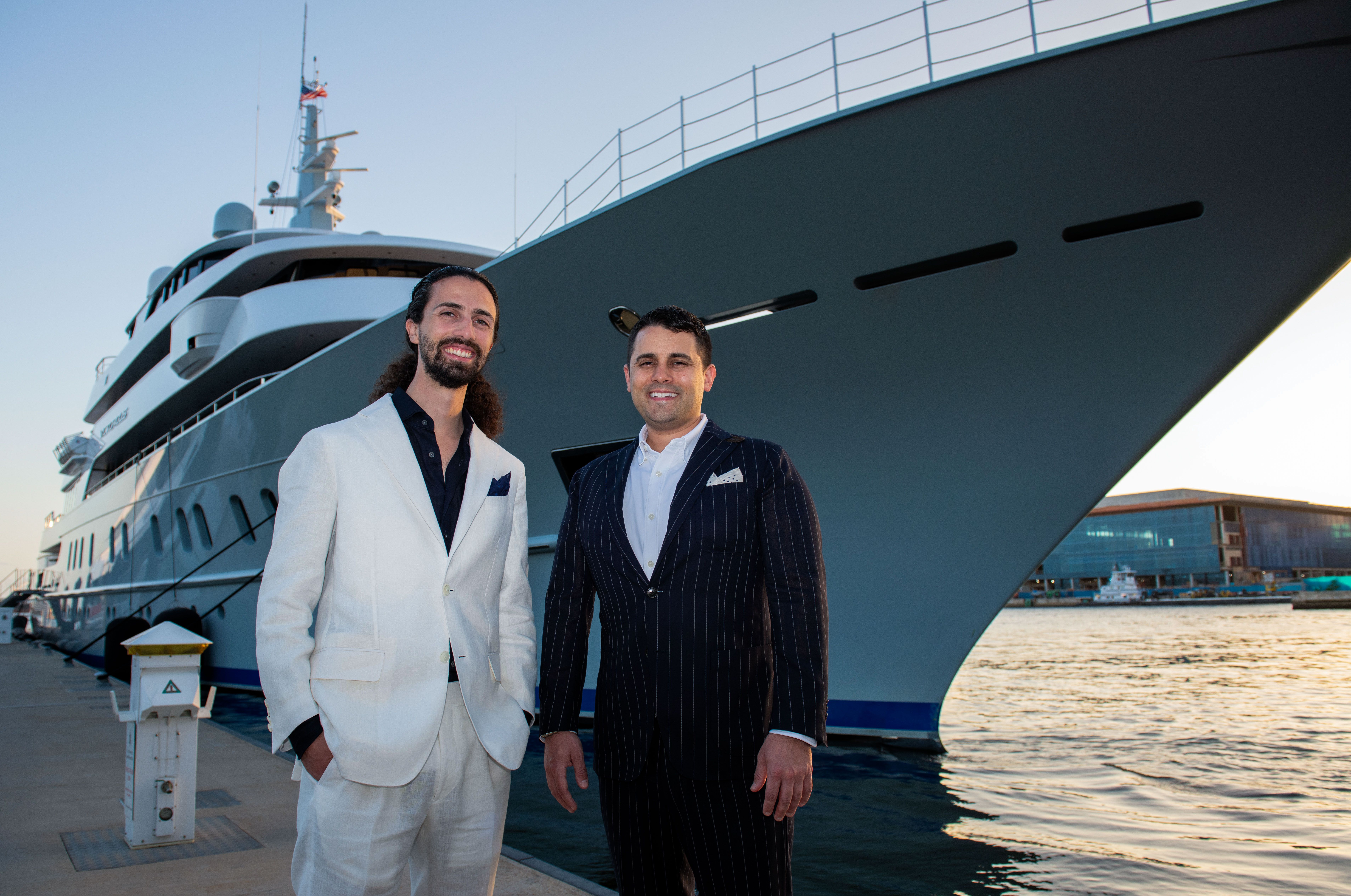 Matthew and Thomas Locastro stand in front of the docked megayacht Victorious