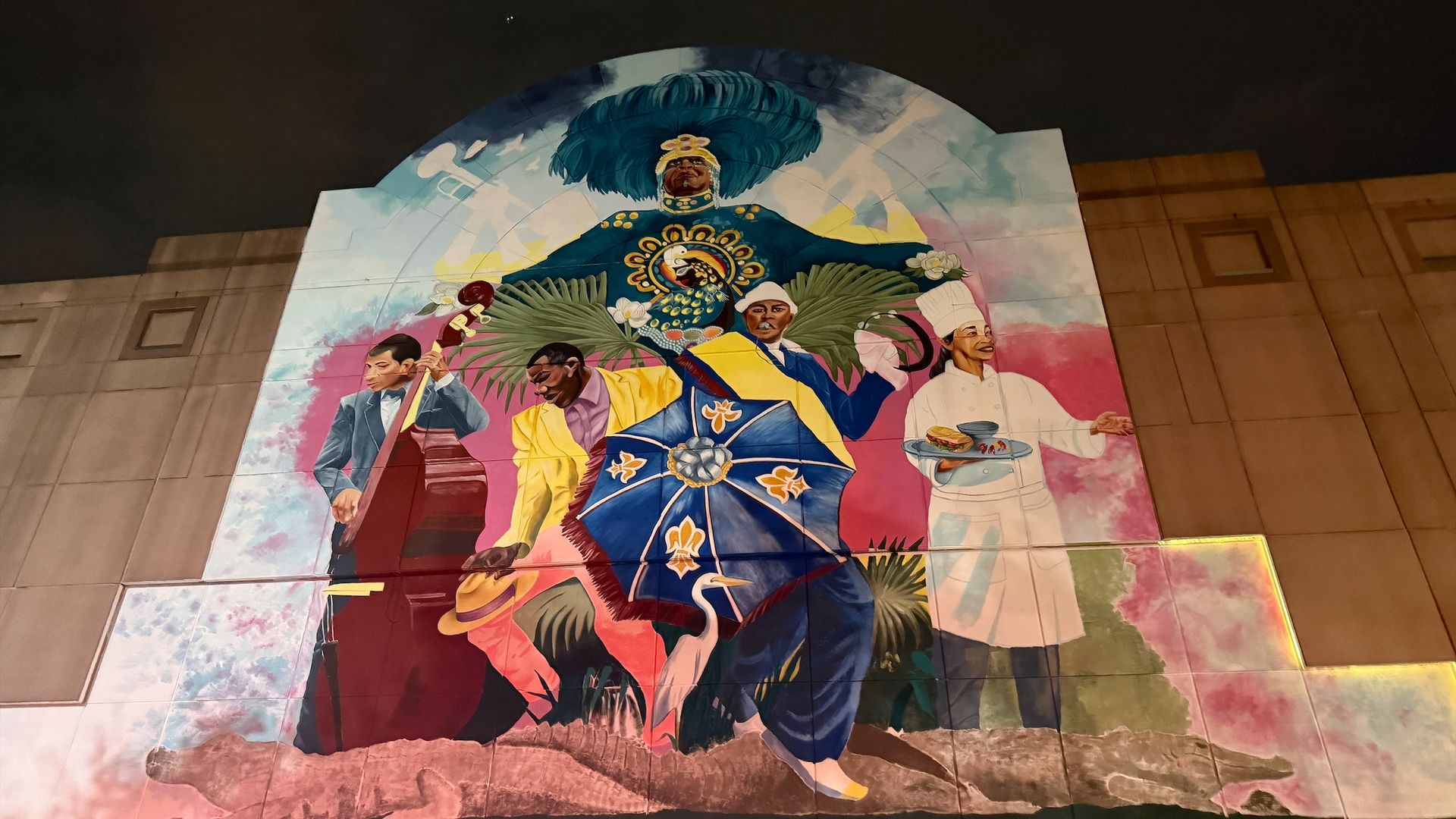 A photo of a mural on a building showing musicians, second-line dancers, a Black Masking Indian and a chef.