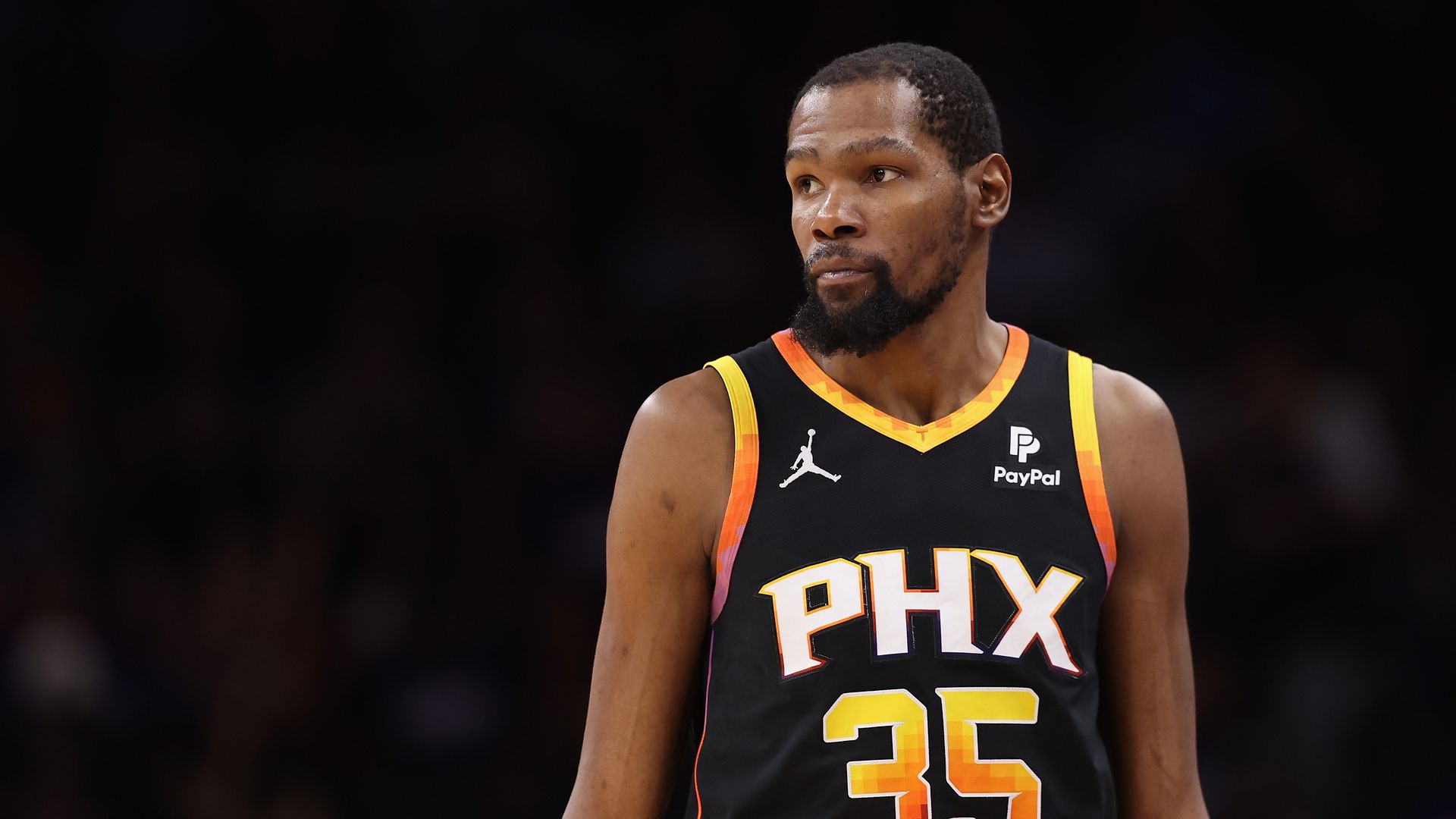 Kevin Durant, wearing a Phoenix Suns jersey, looks away from the camera while playing in a game.