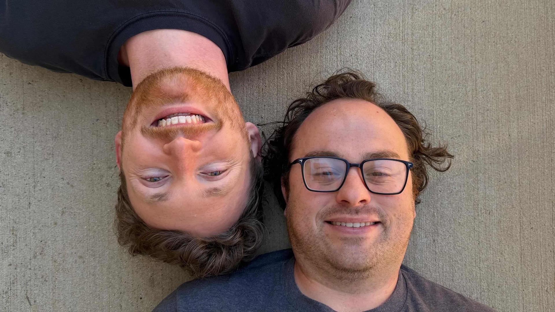 Two people laying on the ground smiling at a camera.