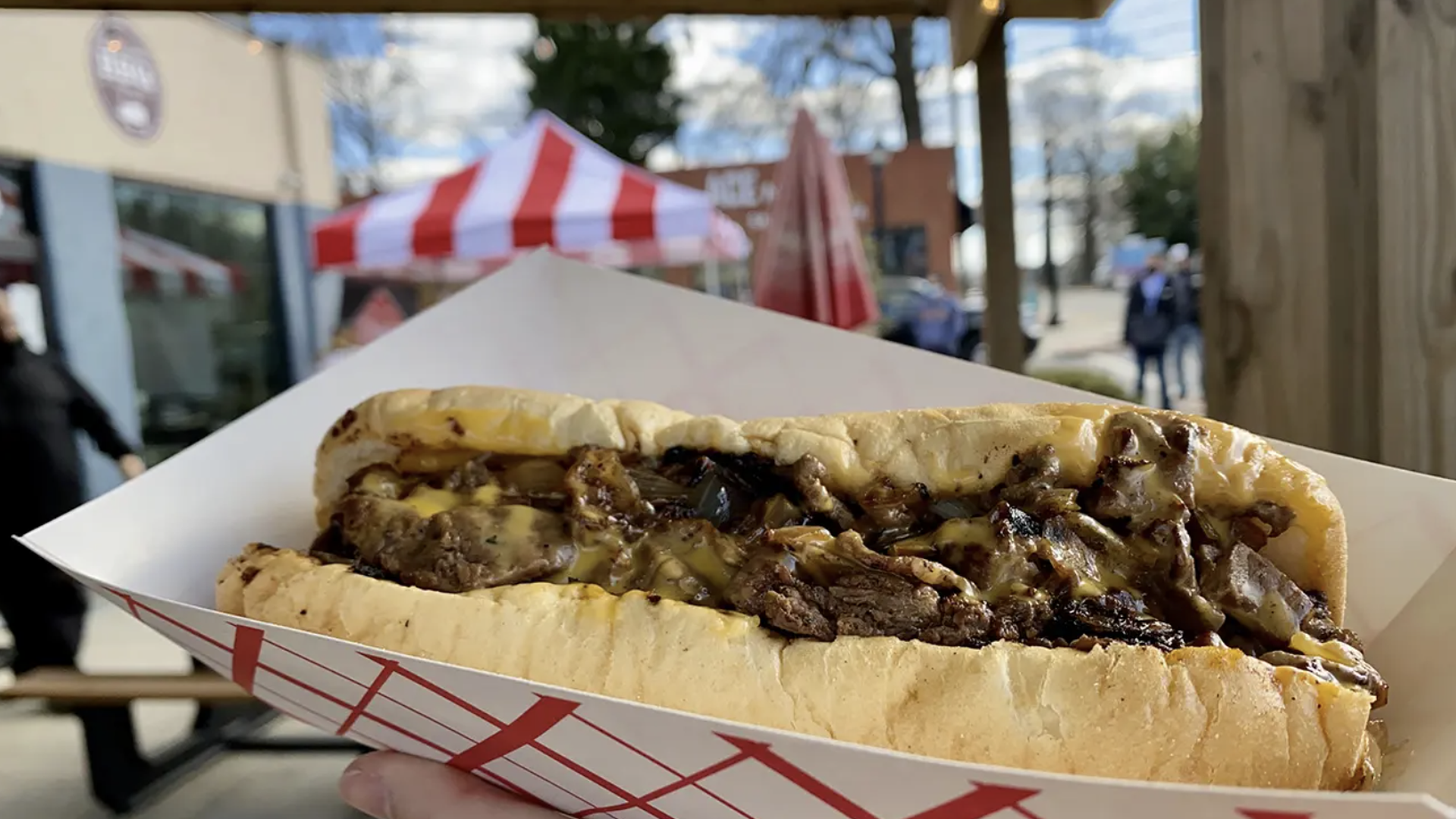 cheesesteak with cheese and onions held up in front of a patio on a sunny day