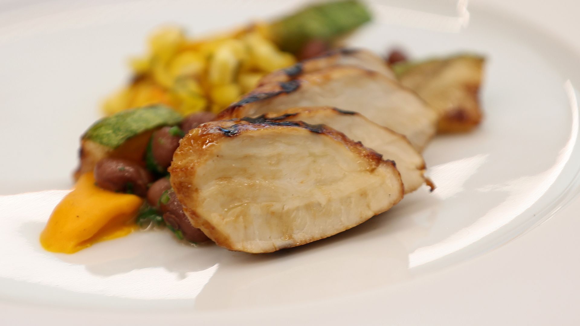 A plate of lab-grown chicken next to roasted vegetables.