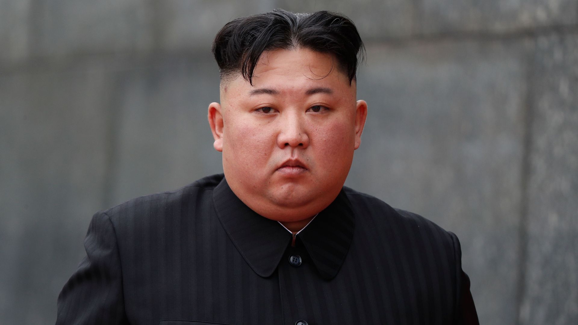 Kim Jong-un standing outside near a stone wall