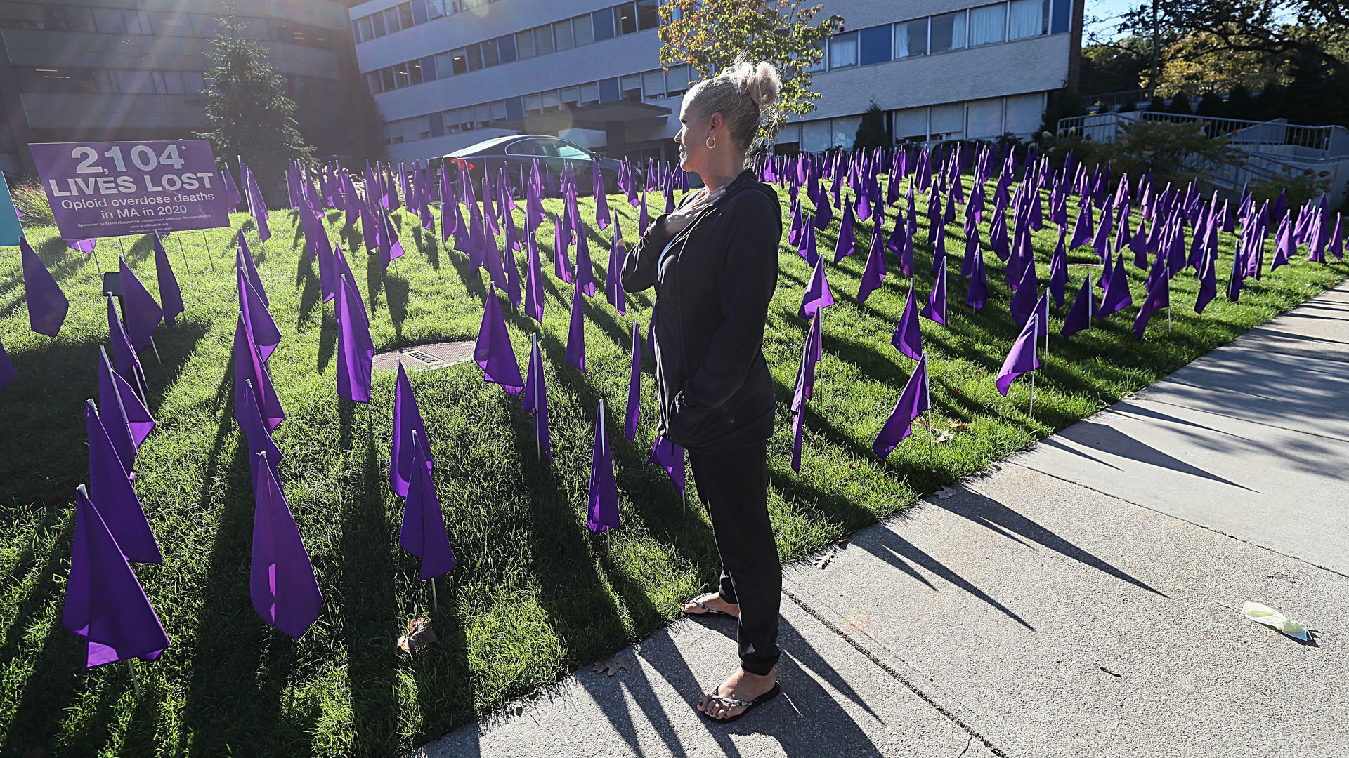 A woman looks over a lawn in front of a hospital with purple flags acknowledging opioid addiction/overdose deaths