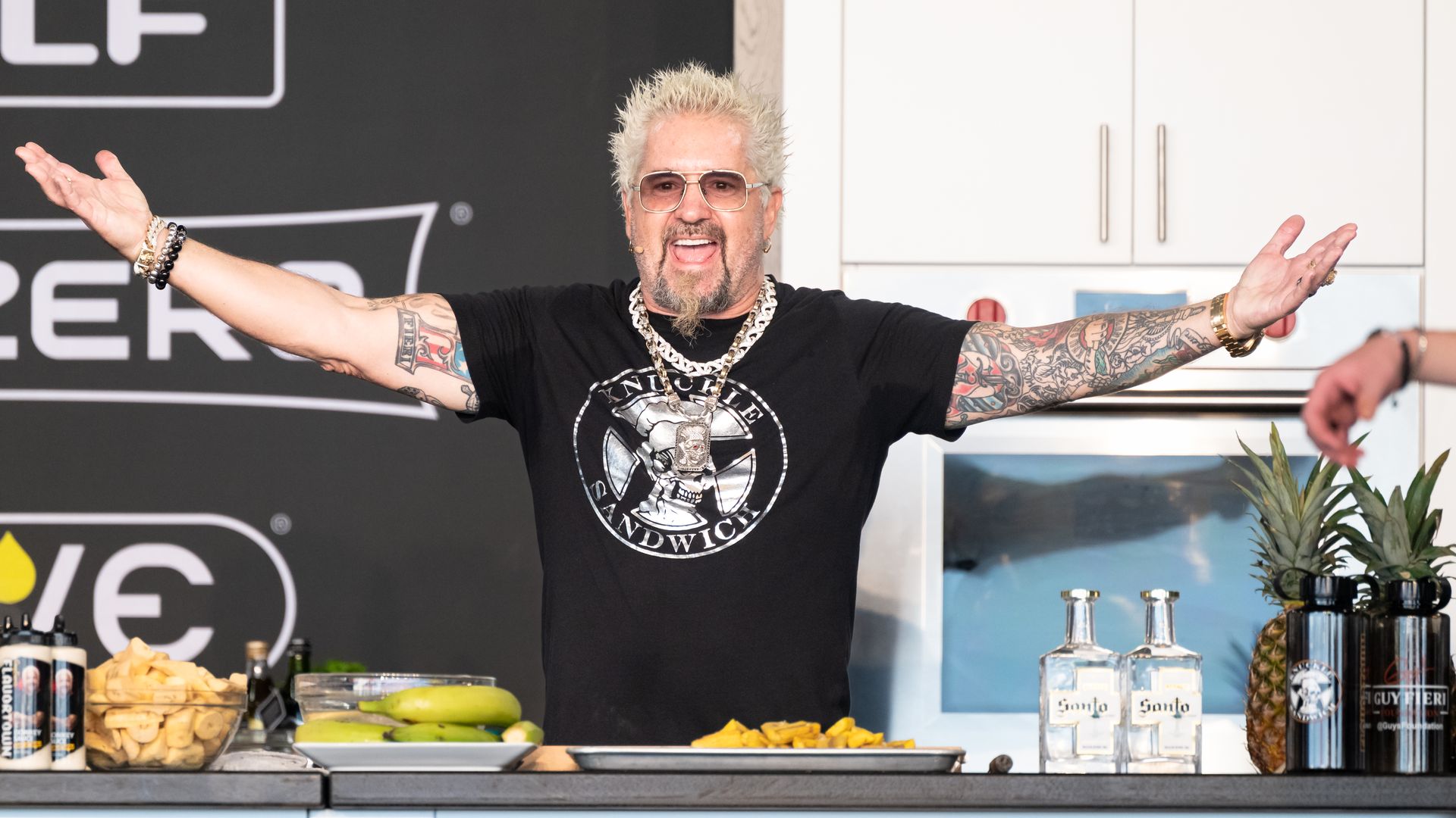 Image shows Guy Fieri gesturing at a table.
