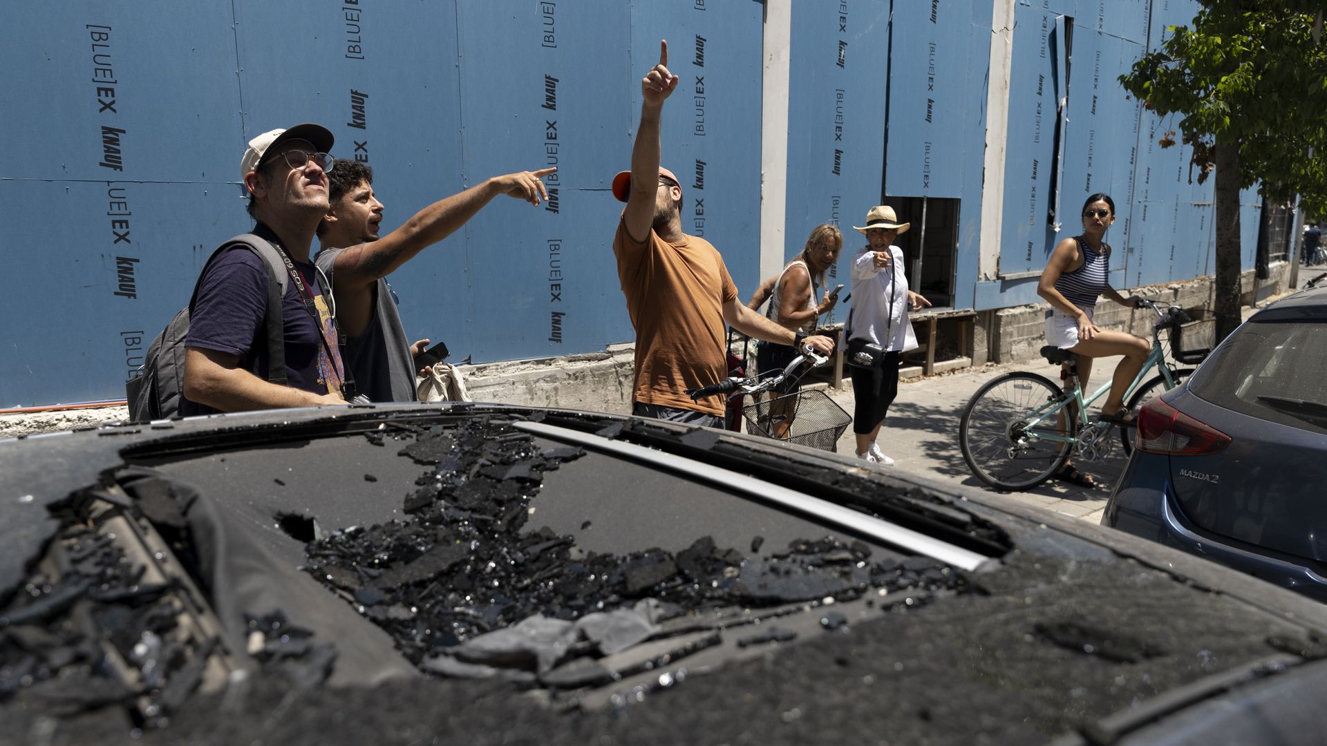 A group of men and women point up at where an drone struck in Tel Aviv, Israel. Broken glass is seen in the foreground.