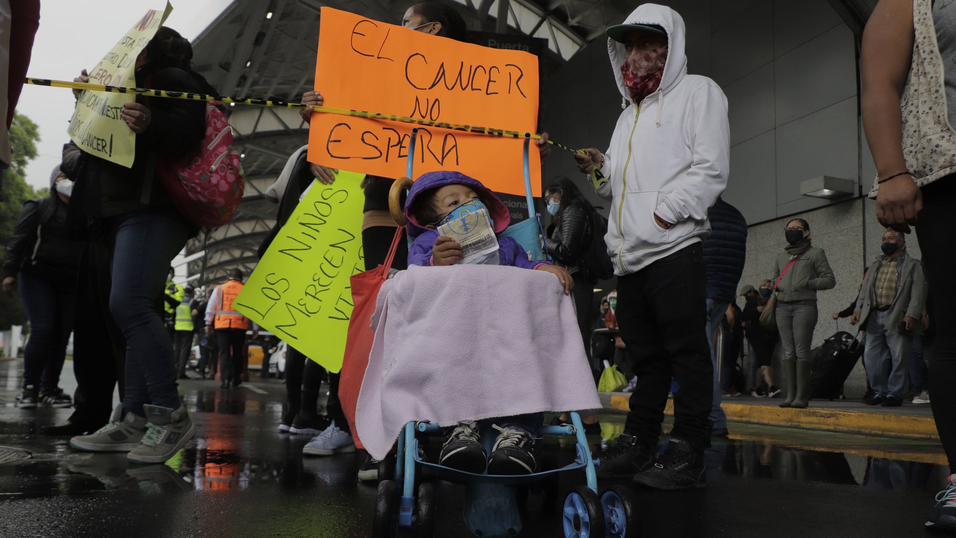 A young cancer patient attends a protest in a wheel chair. Behind her is a sign in Spanish that translates to "Cancer doesn't wait."