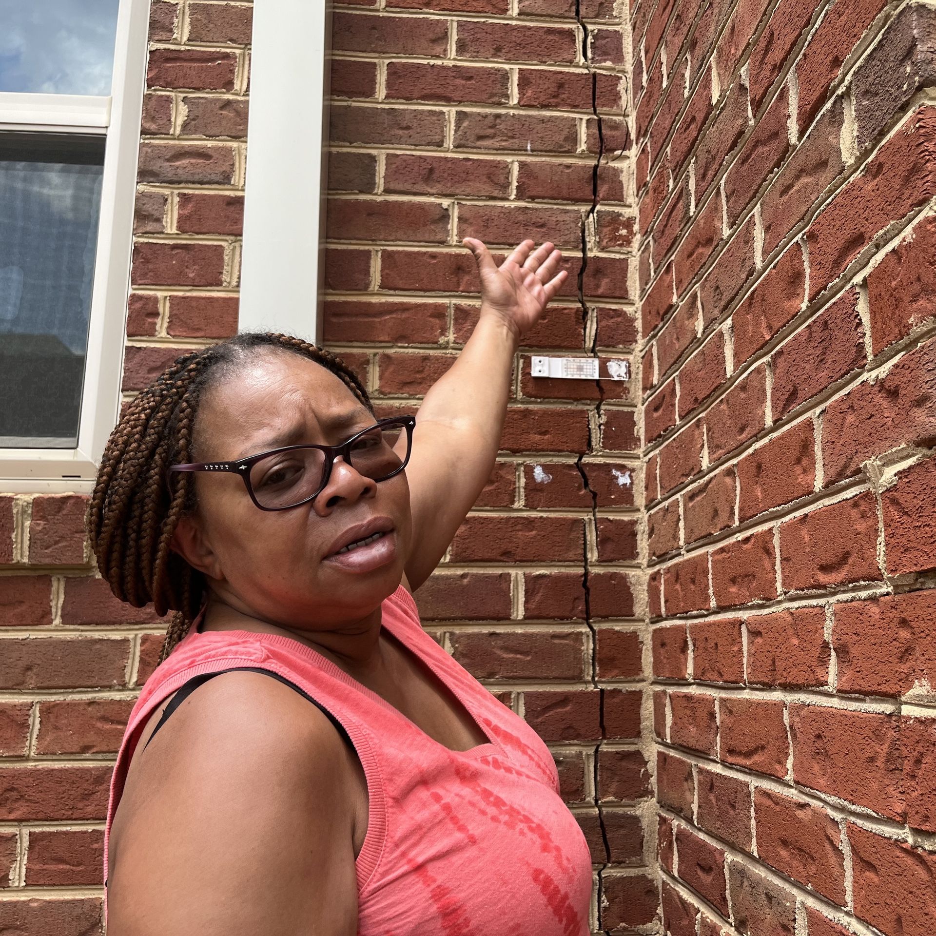 Homeowner points to a crack in the brick facade of building