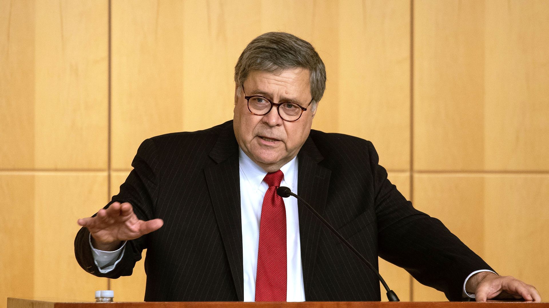 In this image, Barr speaks in a suit and tie from behind a podium.