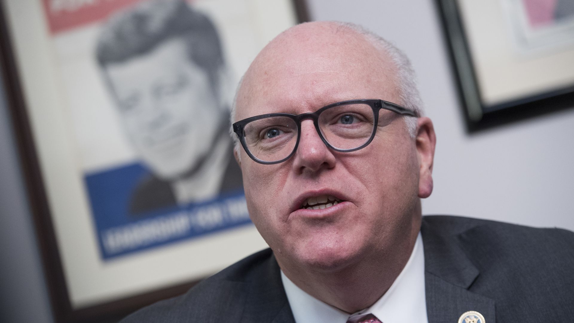 Former Rep. Joe Crowley is seen speaking in front of a "JFK for President" campaign poster.