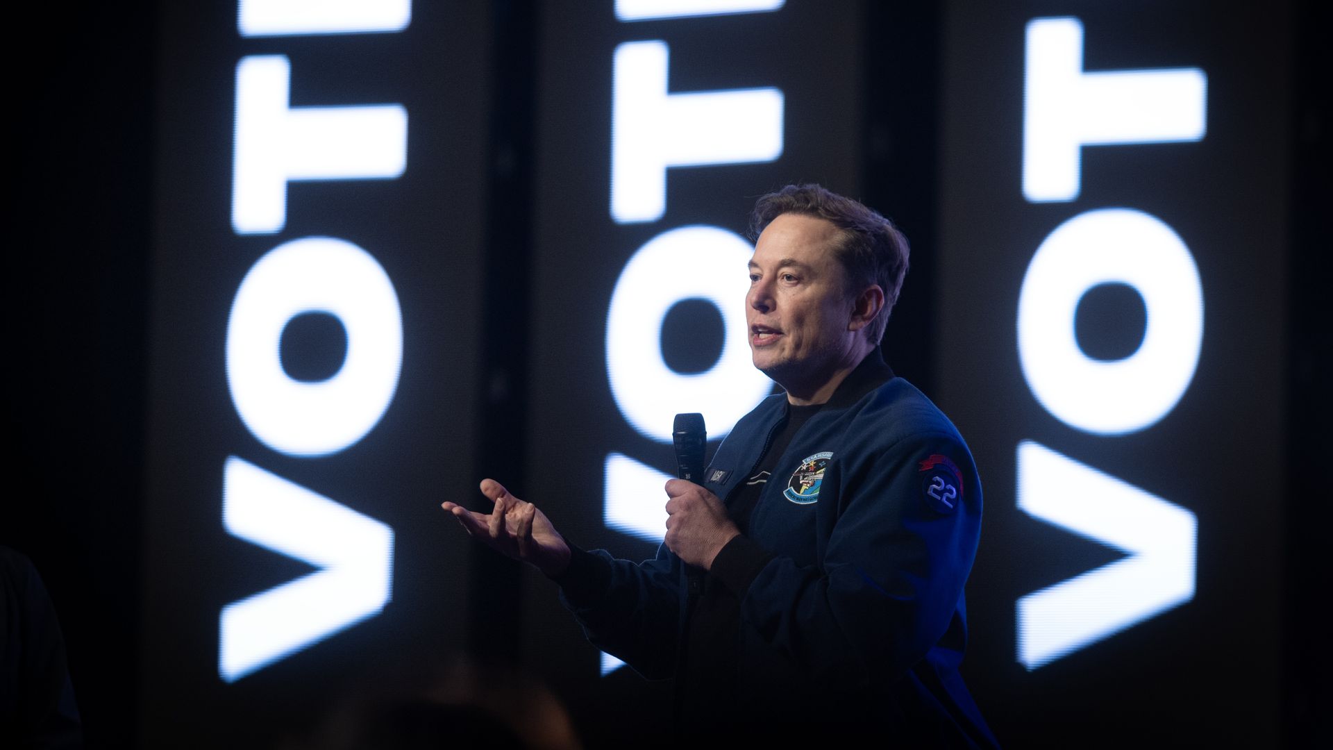 Man at microphone with vote, vote, vote behind him