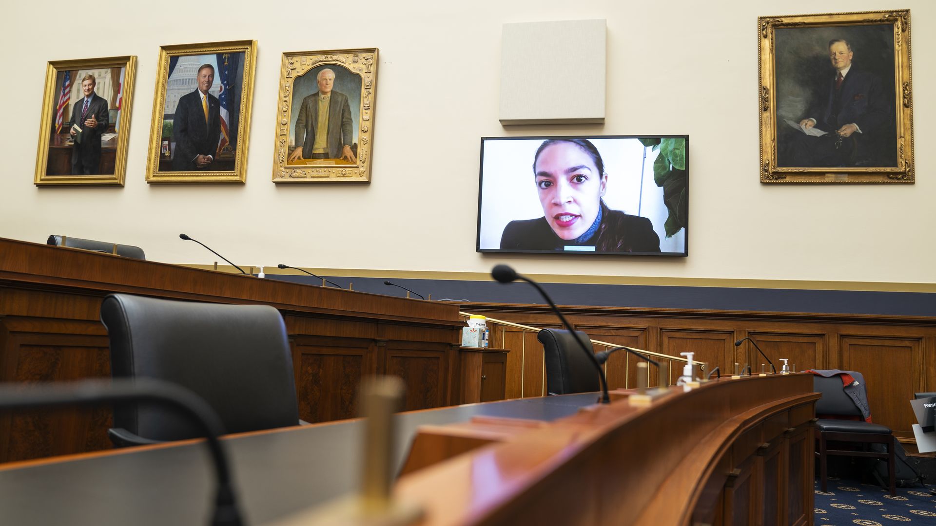 Rep. Alexandria Ocasio-Cortez is seen on a TV monitor as she beams into a House hearing.