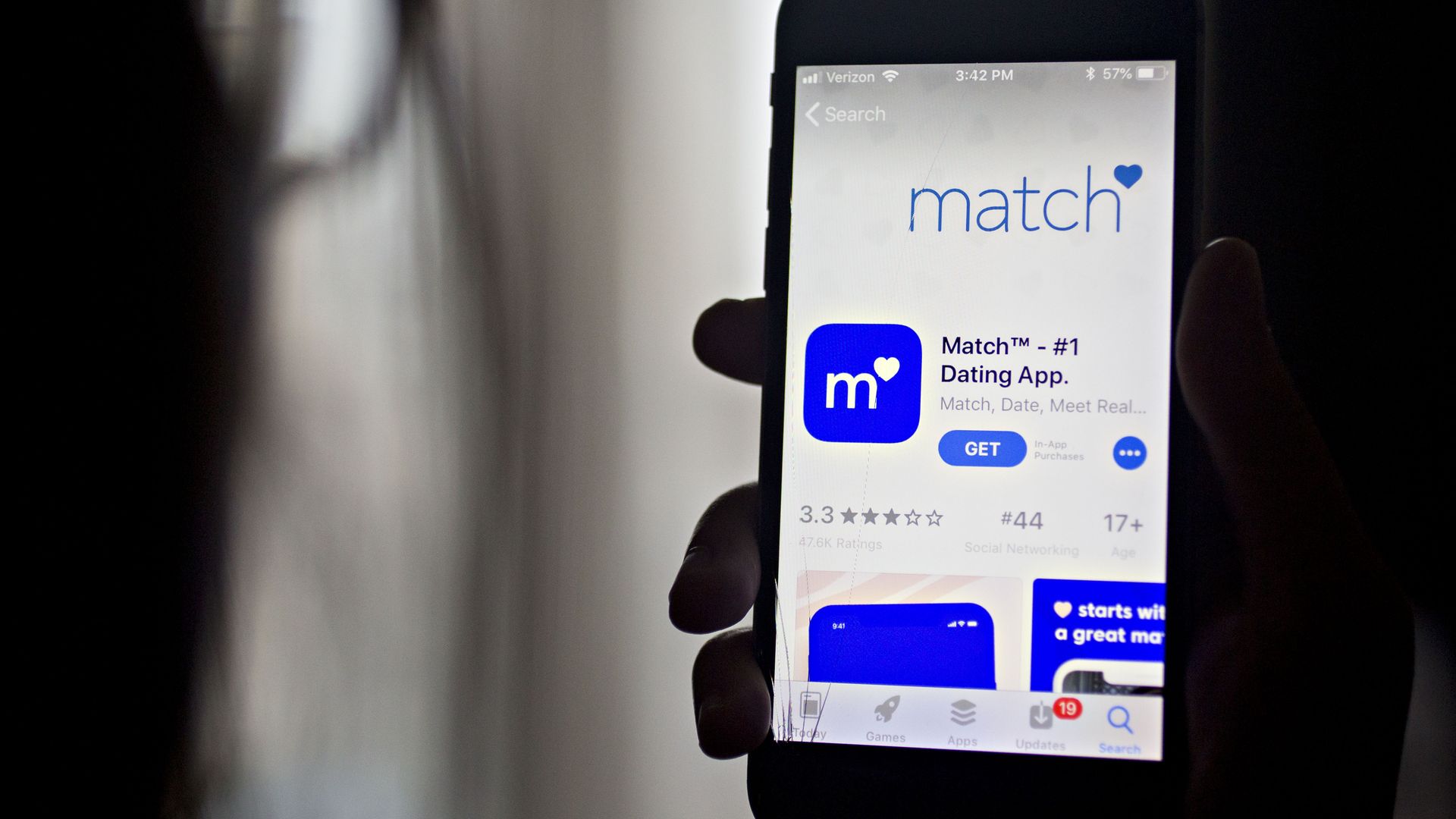 Photo of a hand holding a phone with the Match app details from the App Store on the screen