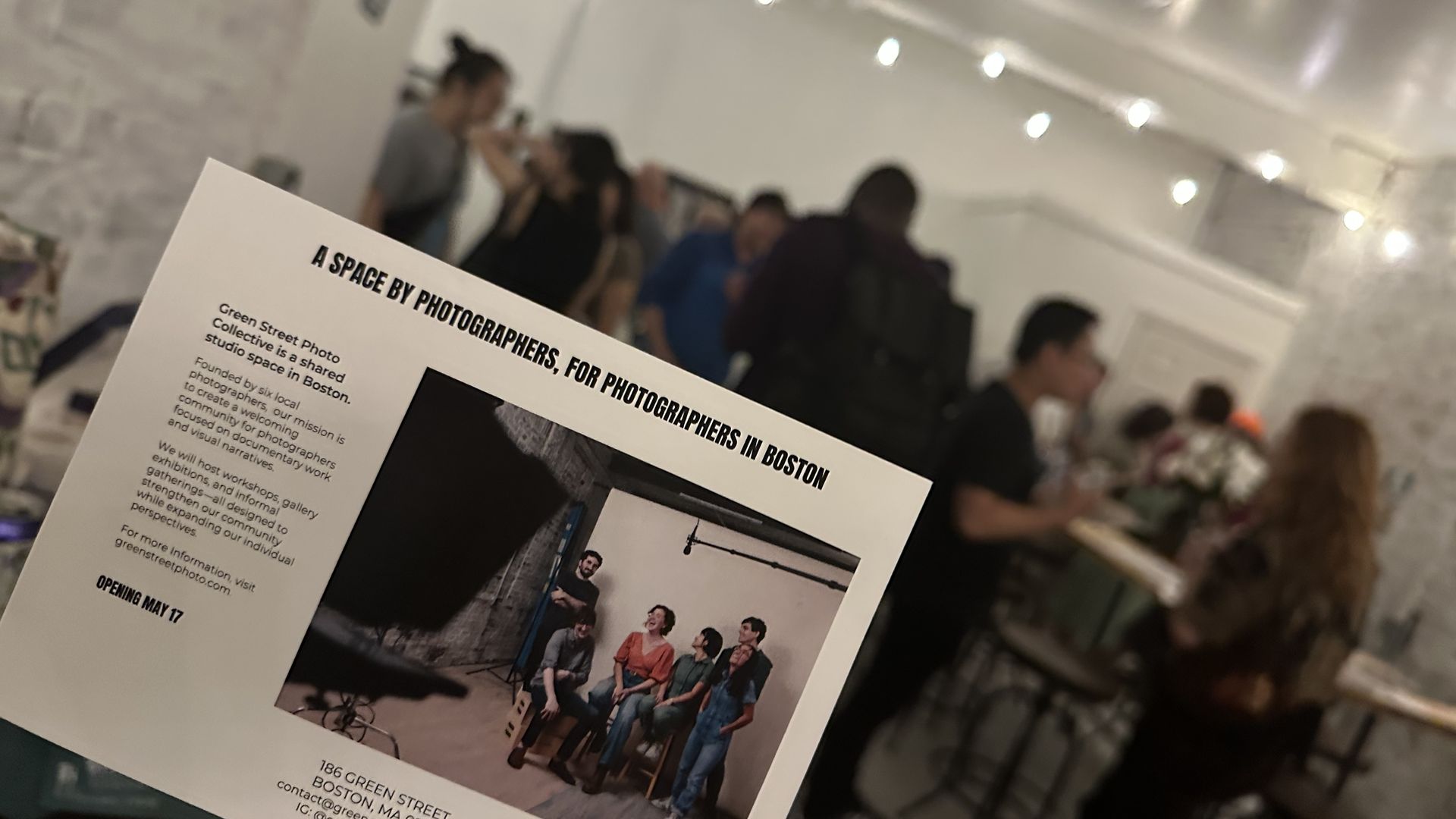 A picture of a postcard explaining the Green Street Collective for photographers with a crowd of attendees in the background of the space.