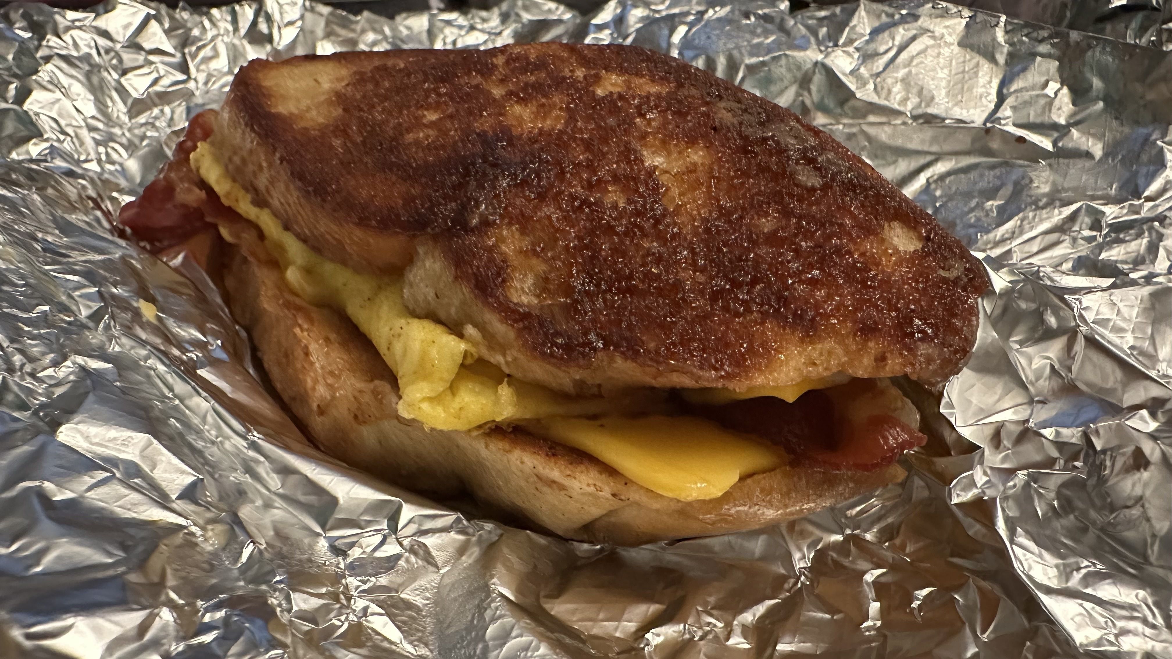 A toasted sandwich with a dark, crispy crust and gooey melted cheese spilling from between the bread, resting on crinkled aluminum foil.