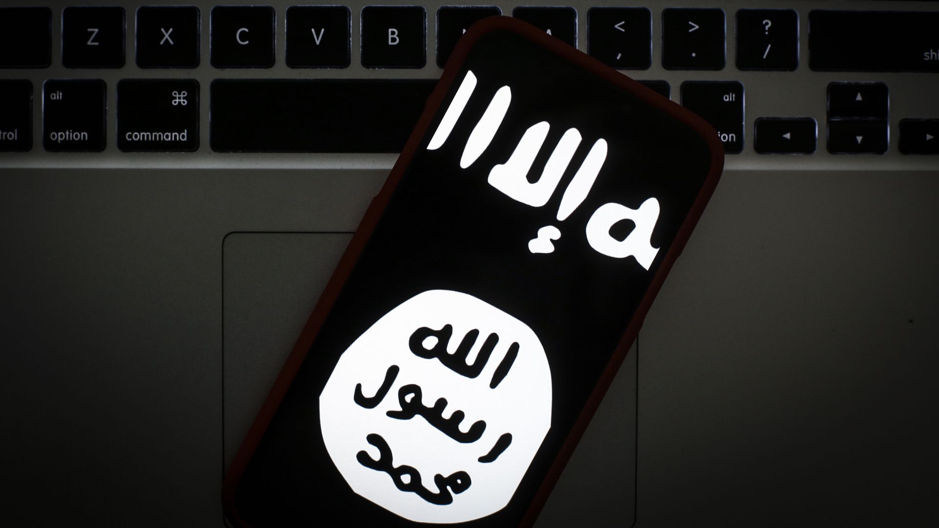 Photo of a phone screen showing the black and white ISIS logo as it rests on a keyboard