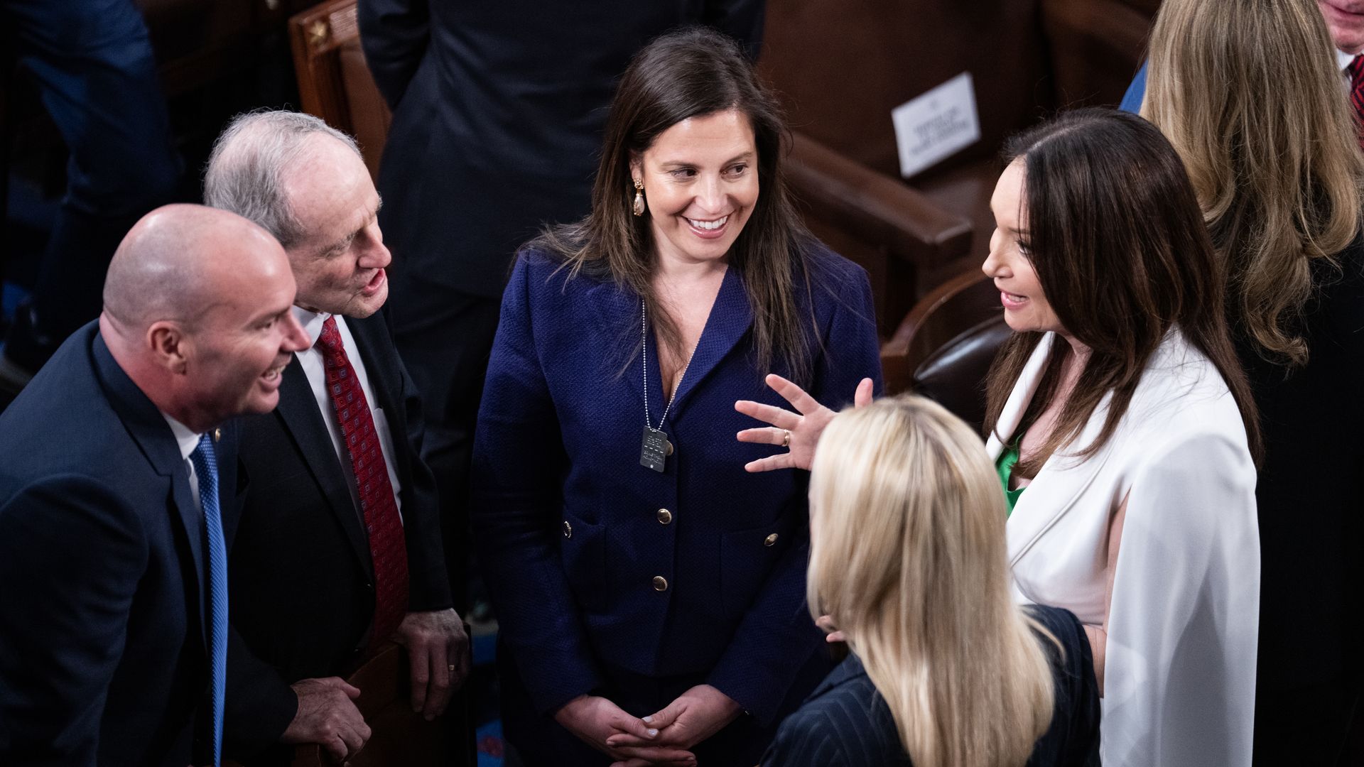 Rep. Elise Stefanik, wearing a blue pantsuit, speaks with others on the House floor.