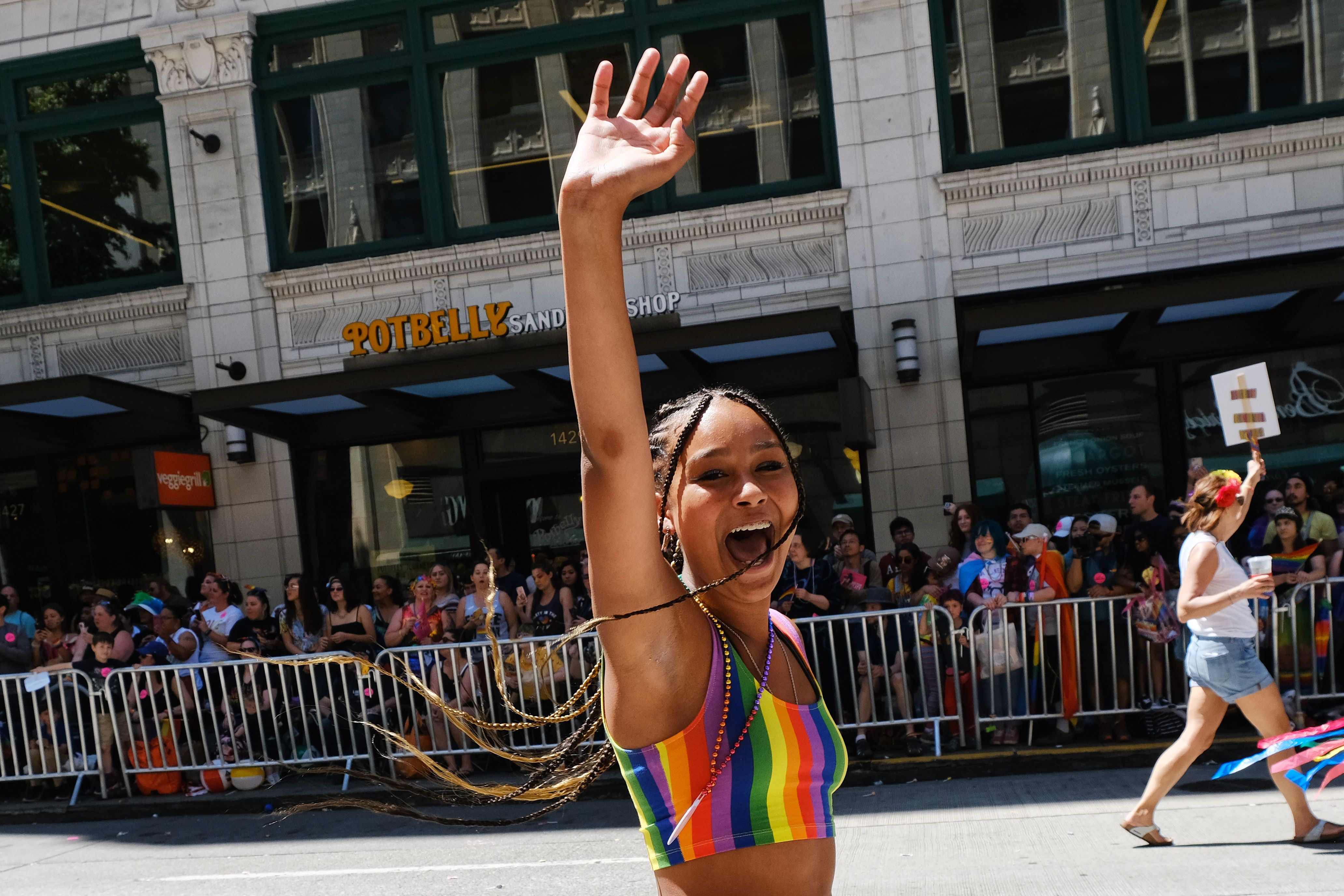 A woman in a rainbow tank top waves joyfully to Pride parade crowds in Seattle. 