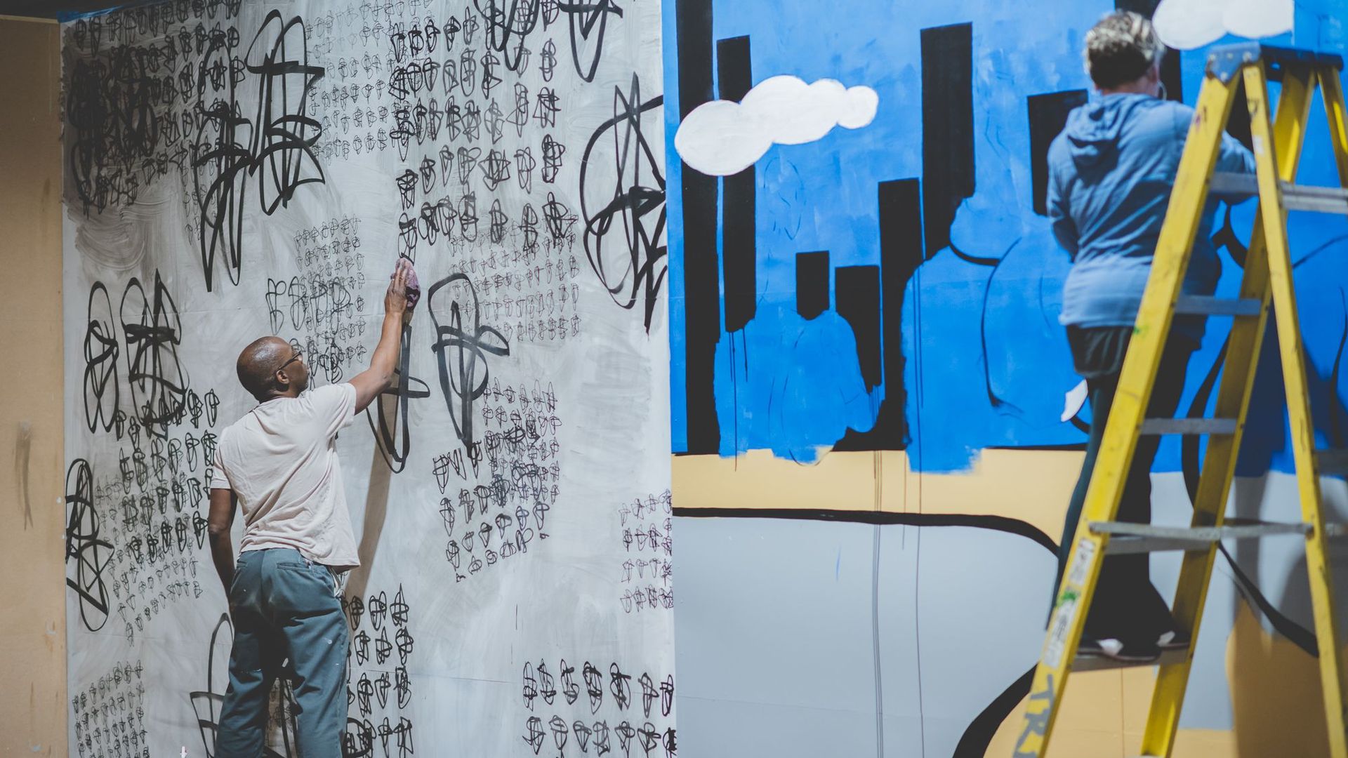 An artist paints on a large plywood canvas he's painted gray.