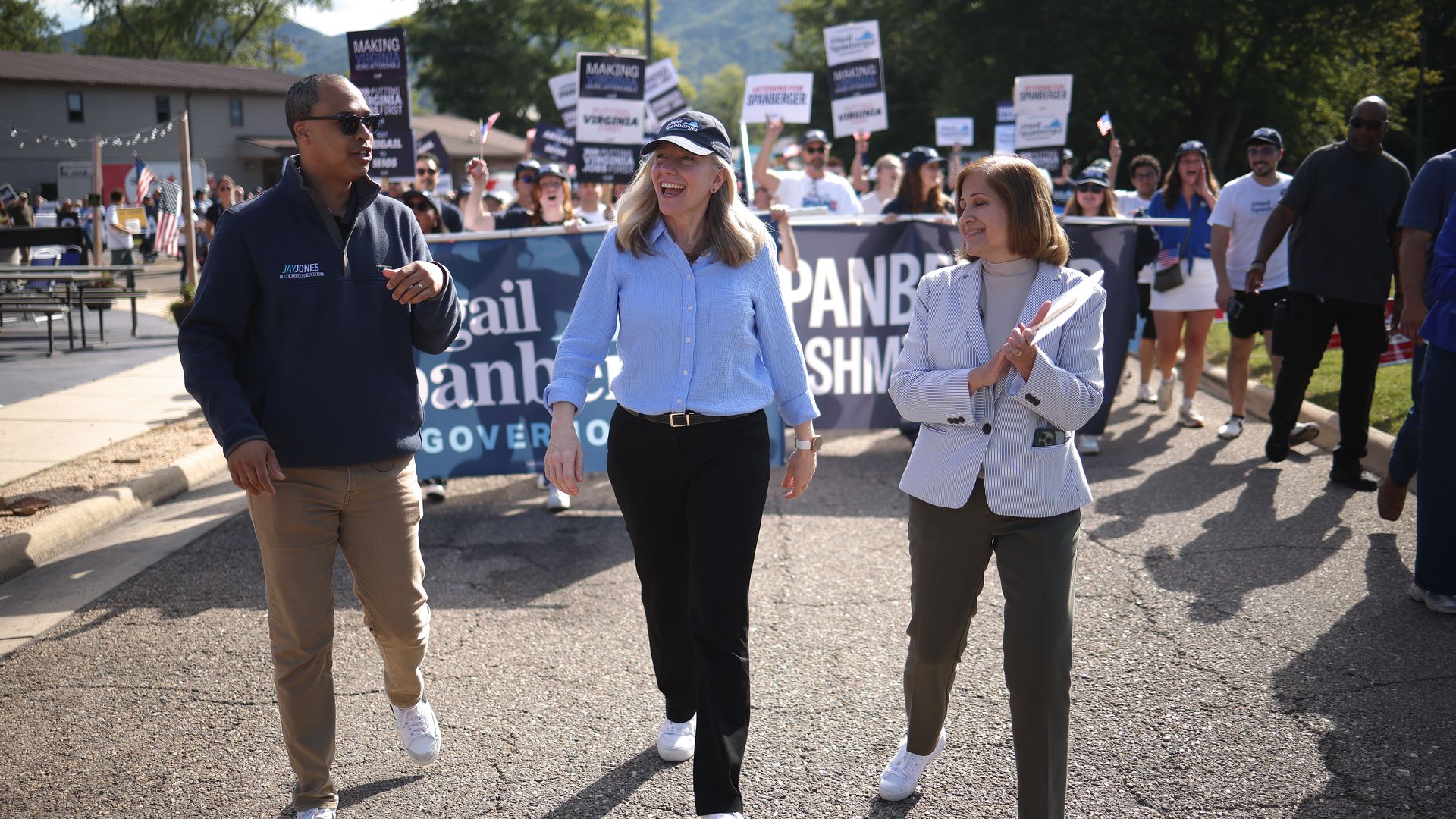 Jay Jones, Abigail Spanberger and Ghazala Hashmi walking side by side in a parade with a blue banner with their names on it behind them