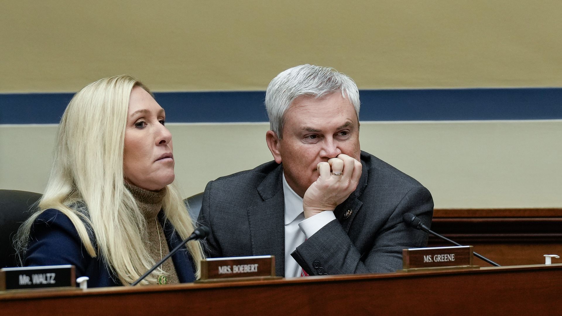 Rep. Marjorie Taylor Greene, wearing a blue blazer and brown turtleneck sweater, and Oversight Commmittee Chair James Comer, wearing a gray suit, sitting at a committee hearing.