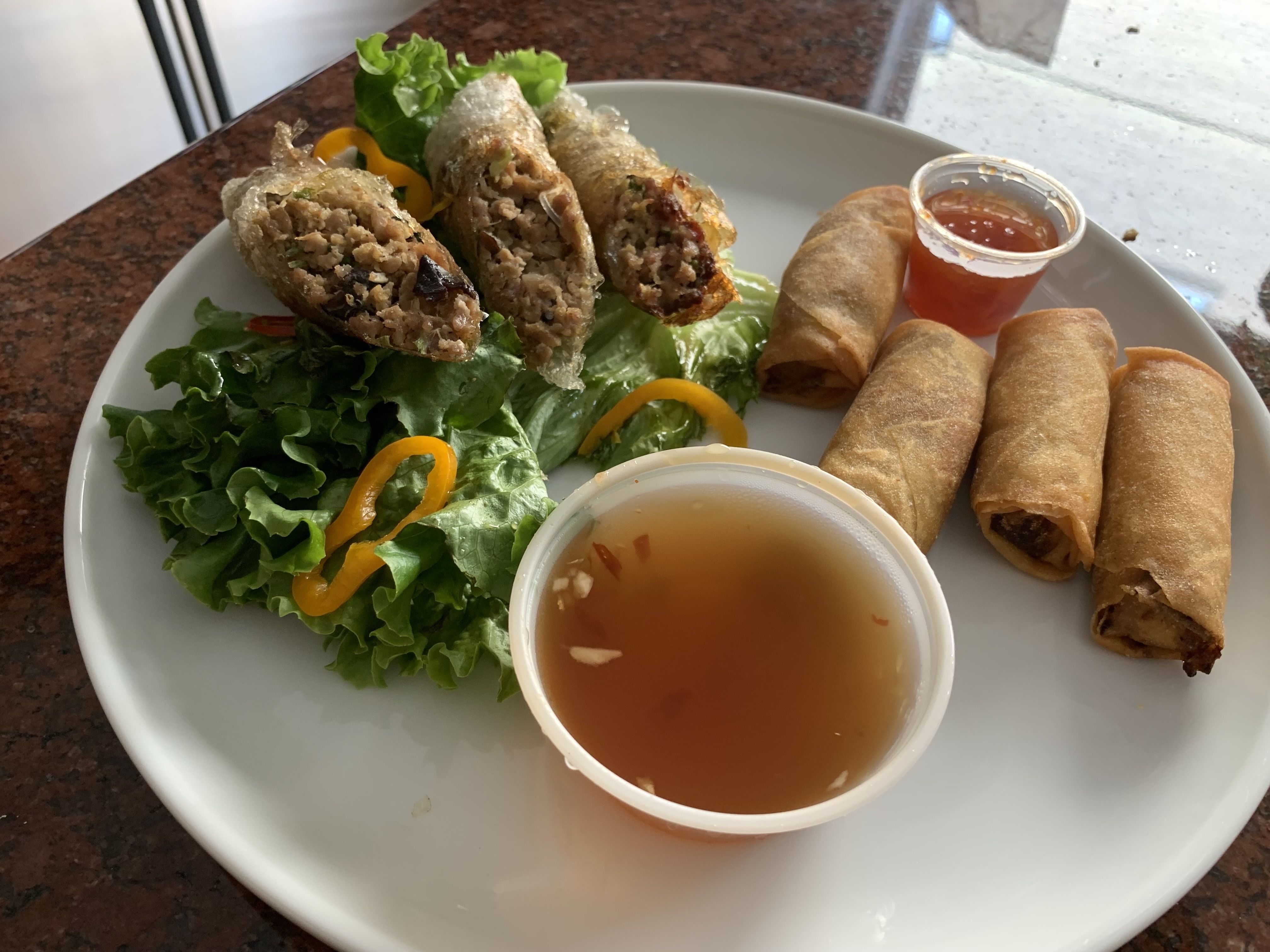 Photo of egg rolls on a plate with dipping sauce. 