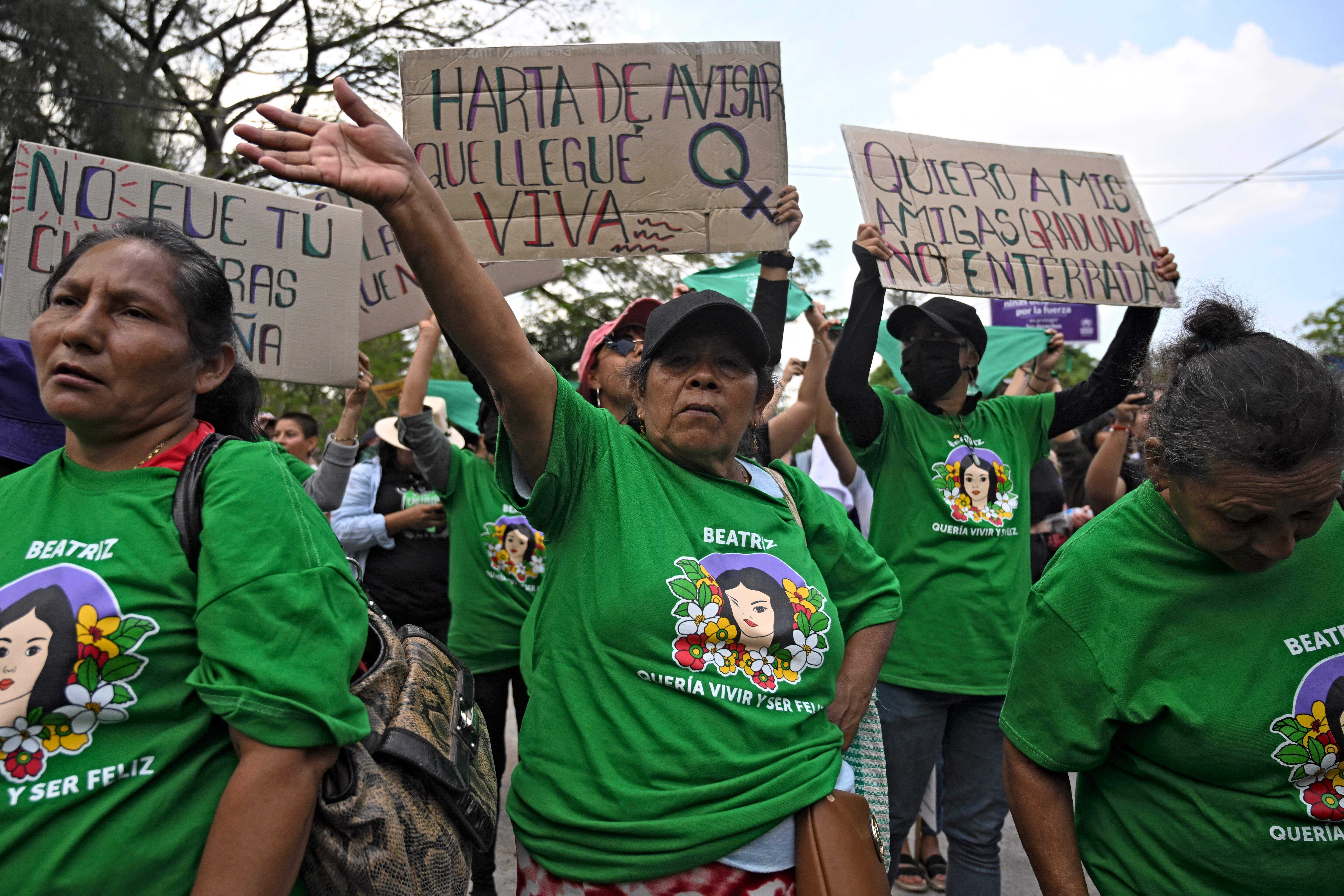 Women in green march in San Salvador during International Women's Day, holding cardboard signs protesting violence against women