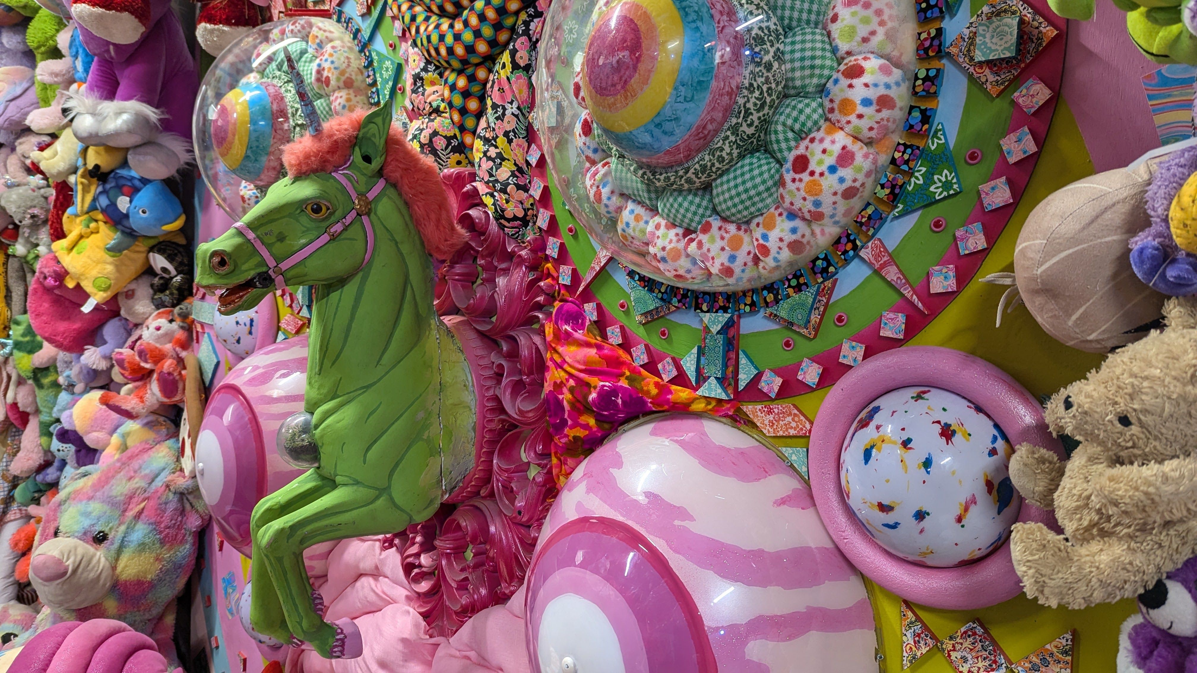 A green carousel horse leaps out of a wall covered in toys and 