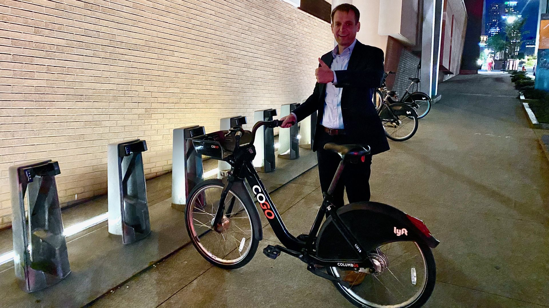 Axios publisher Nick Johnston gives a "thumbs up" while posing next to a CoGo bike.
