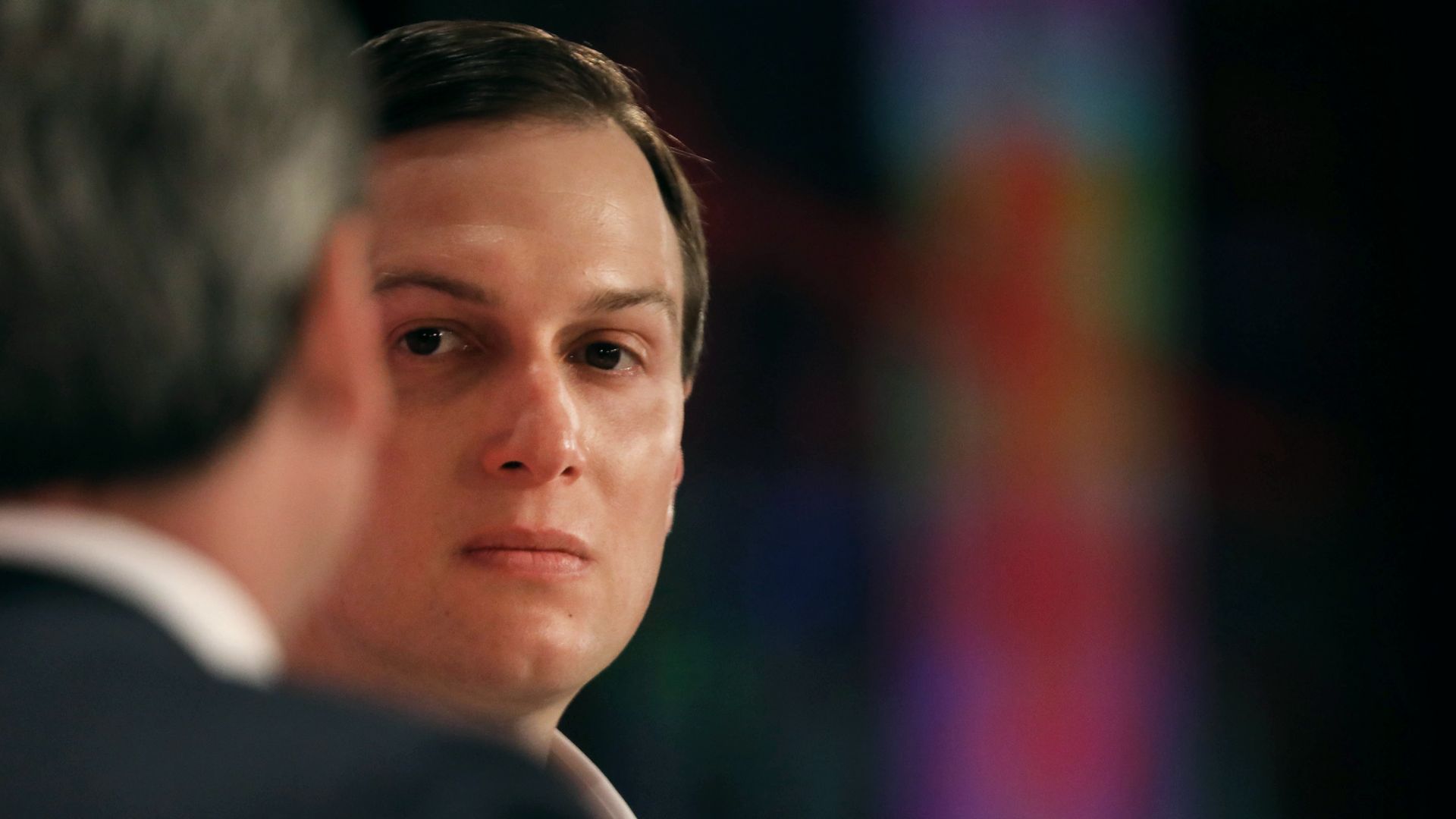 Jared Kushner on stage at an event looking very serious. The back of an interviewer's head is in the foreground.