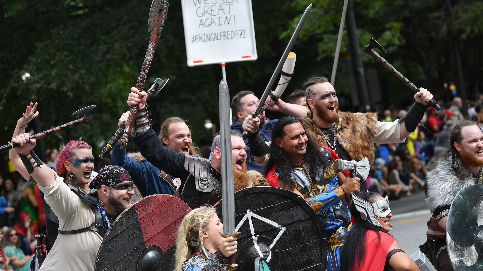 A group of people dressed as vikings and holding a sign saying "Make Wessex Great Again" pose for a photographer during a parade