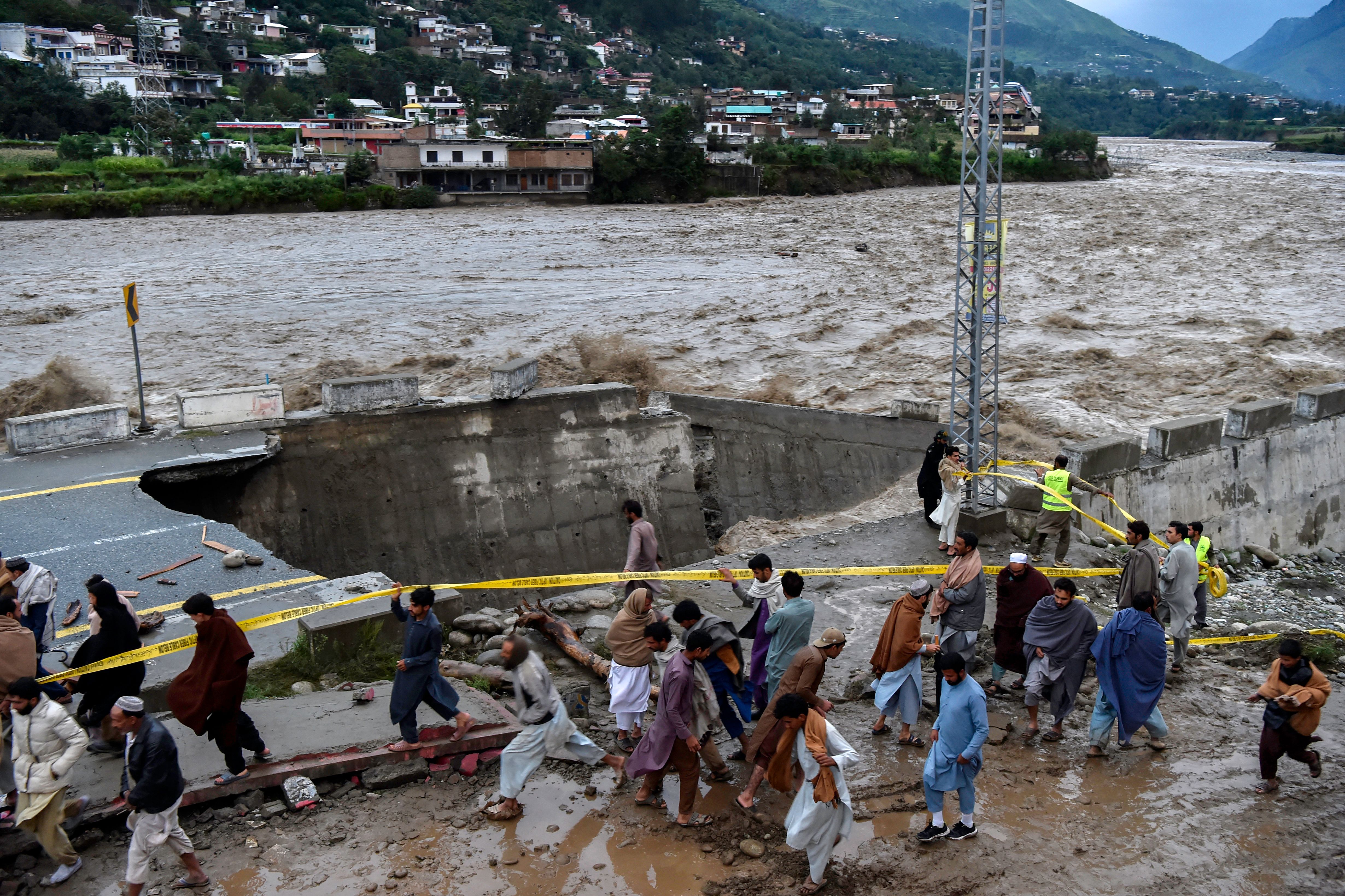 People gather in front of a road damaged by flood waters following heavy monsoon rains in Madian area in Pakistan's northern Swat Valley on August 27.