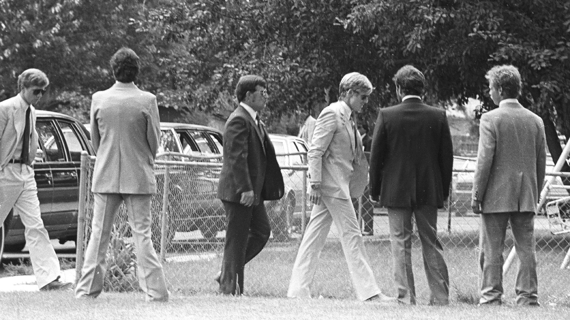 Black and white photo of Robert Redford and five other men wearing suits at an outdoor funeral.