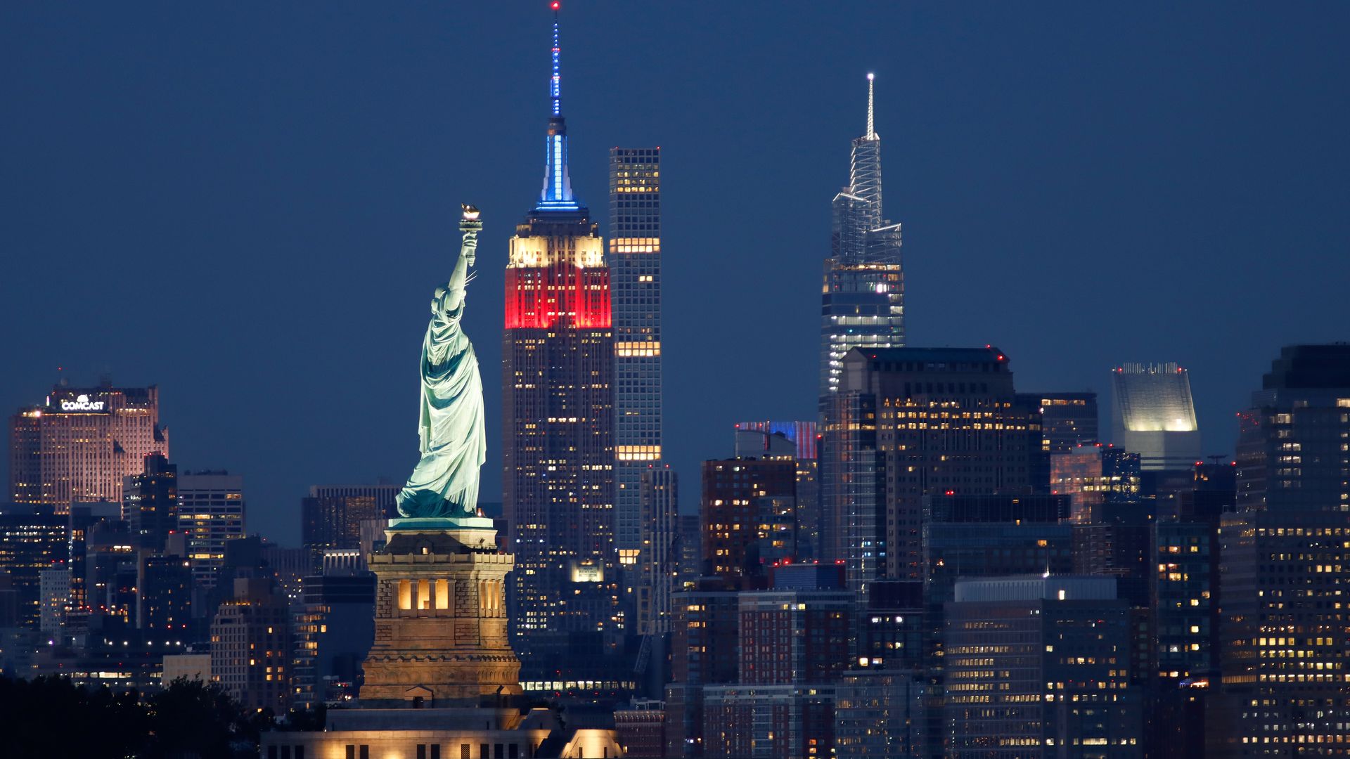 Photo of the New York City skyline at night, with the Statue of Liberty lit up in the middle