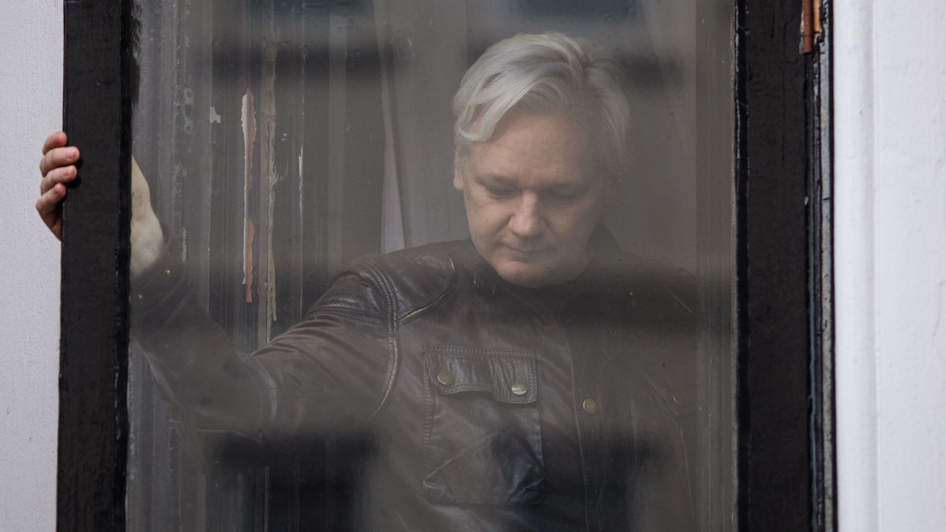 Julian Assange seen through a window, looking down.
