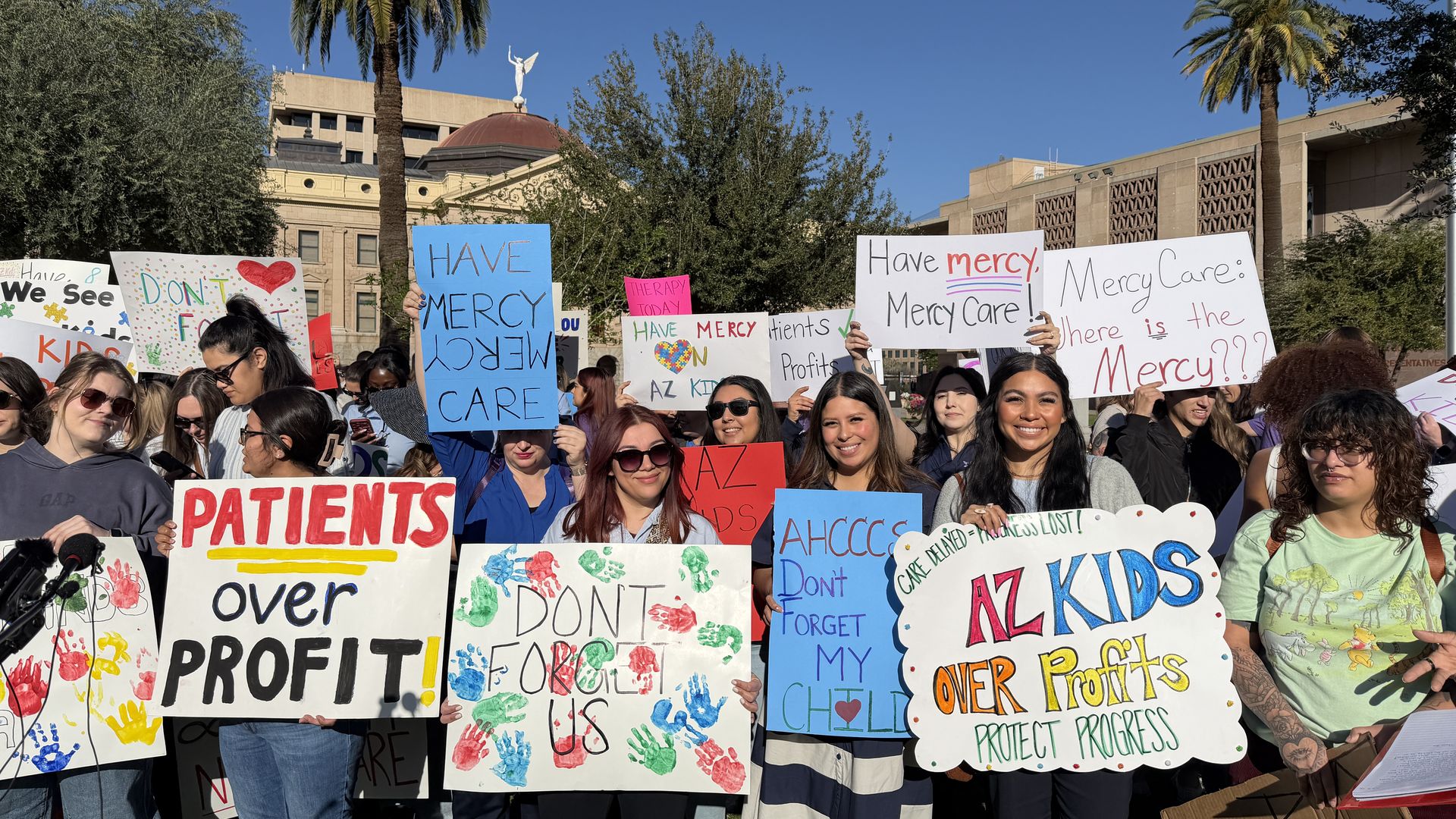 A group of diverse protestors hold colorful signs with messages like "PATIENTS over PROFIT!", "DON'T FORGET US", and "AZ KIDS OVER Profits" in front of a government building with palm trees and a clear blue sky.