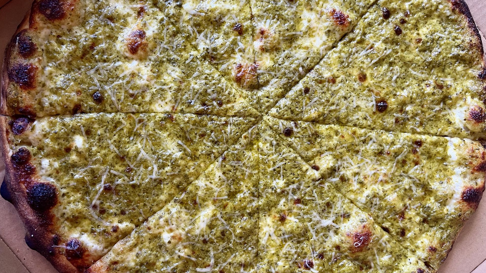 Round pizza with thick, browned crust, covered in green poblano sauce and melted cheese, with visible shredded cheese; sits inside a brown pizza box. The signature poblano pie from Lovers Pizzeria.