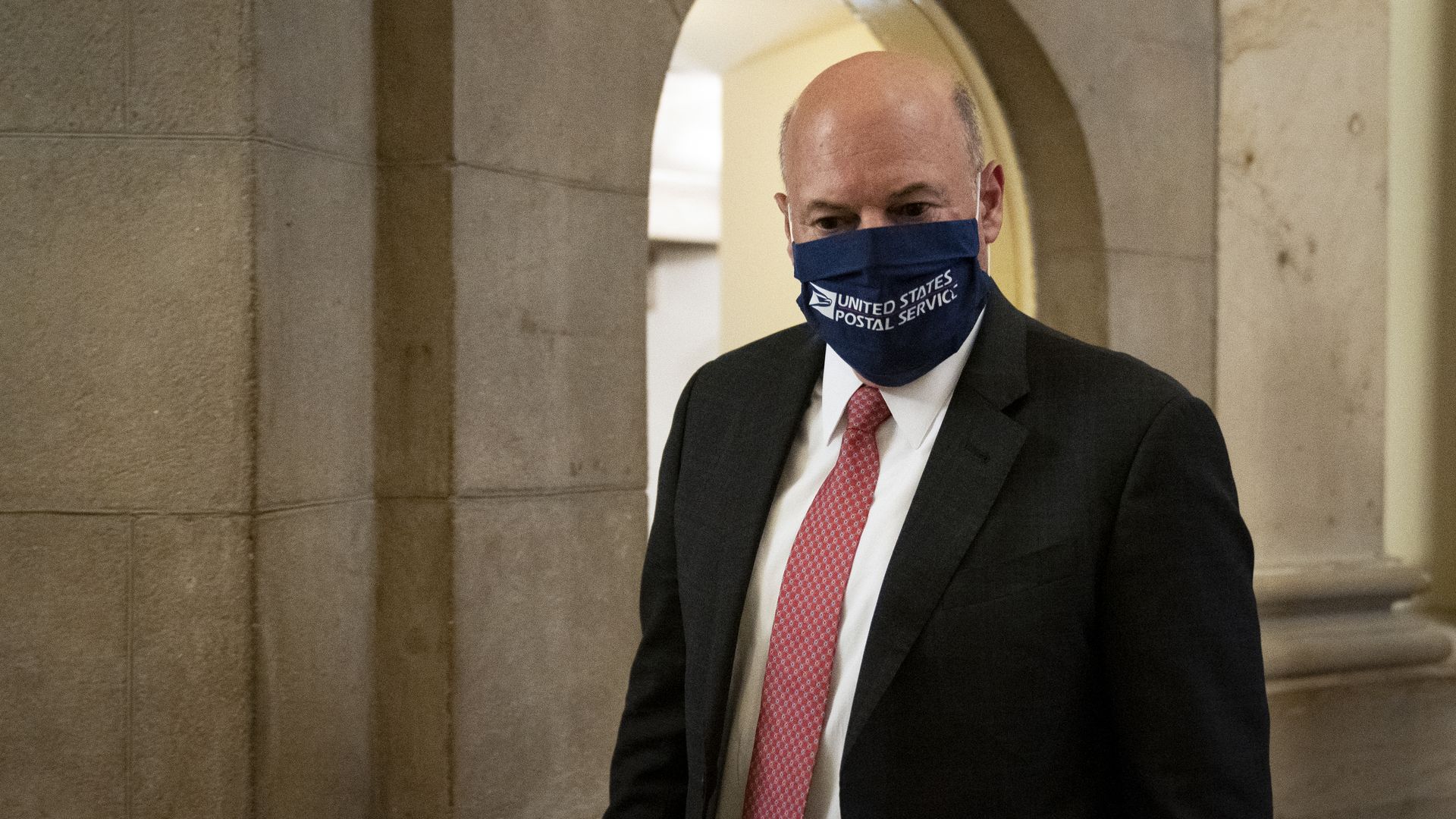 Louis DeJoy wearing a face mask that says "US Postal Service"